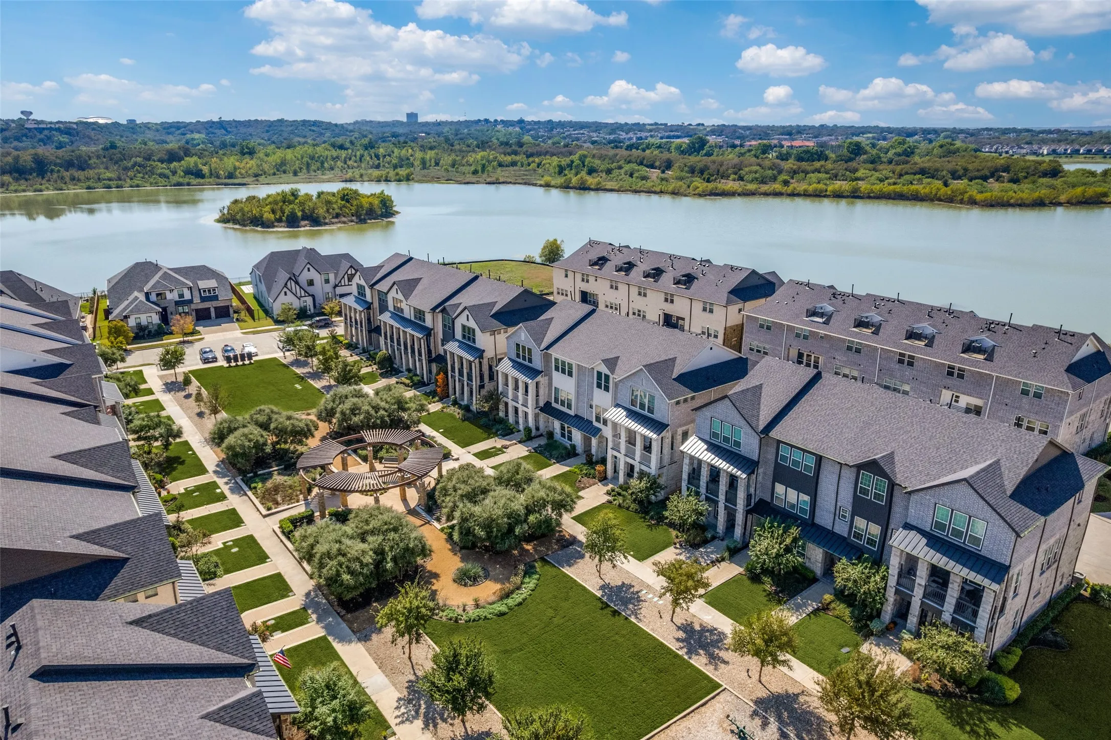 Waterfront community featuring multi-story residences, manicured communal green spaces, and a circular pergola structure