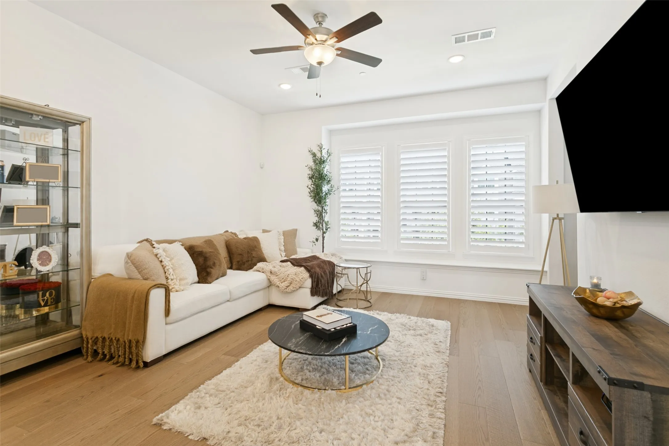 Hardwood-style flooring, recessed lighting, ceiling fan, and multiple windows with plantation shutters
