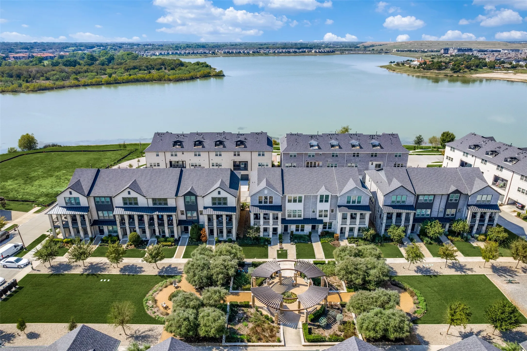Townhomes with gabled roofs, a communal greenspace with landscaped beds, and a lakefront setting