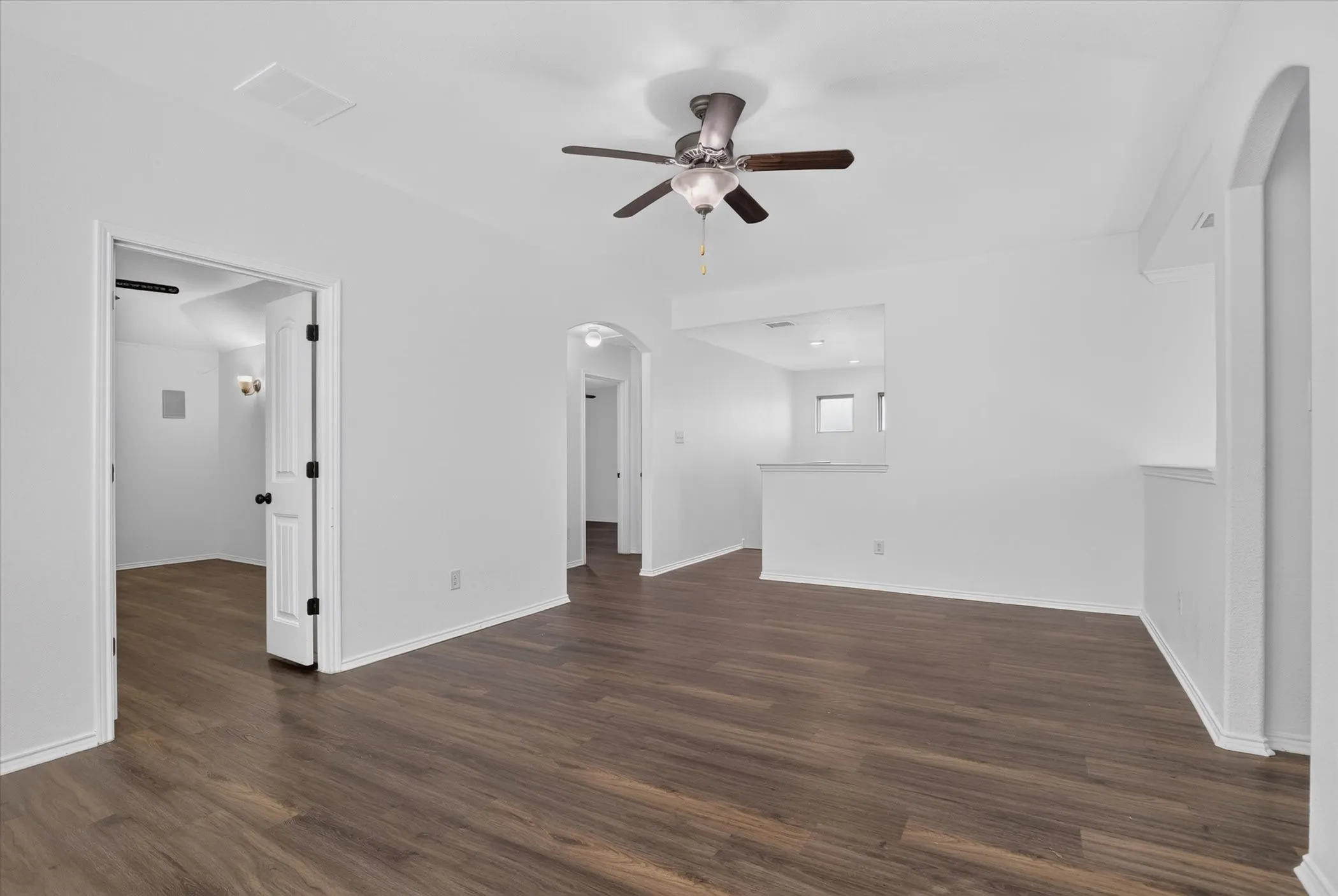Wood-finish flooring throughout, white painted walls, ceiling-mounted fan with integrated lighting, and an arched doorway