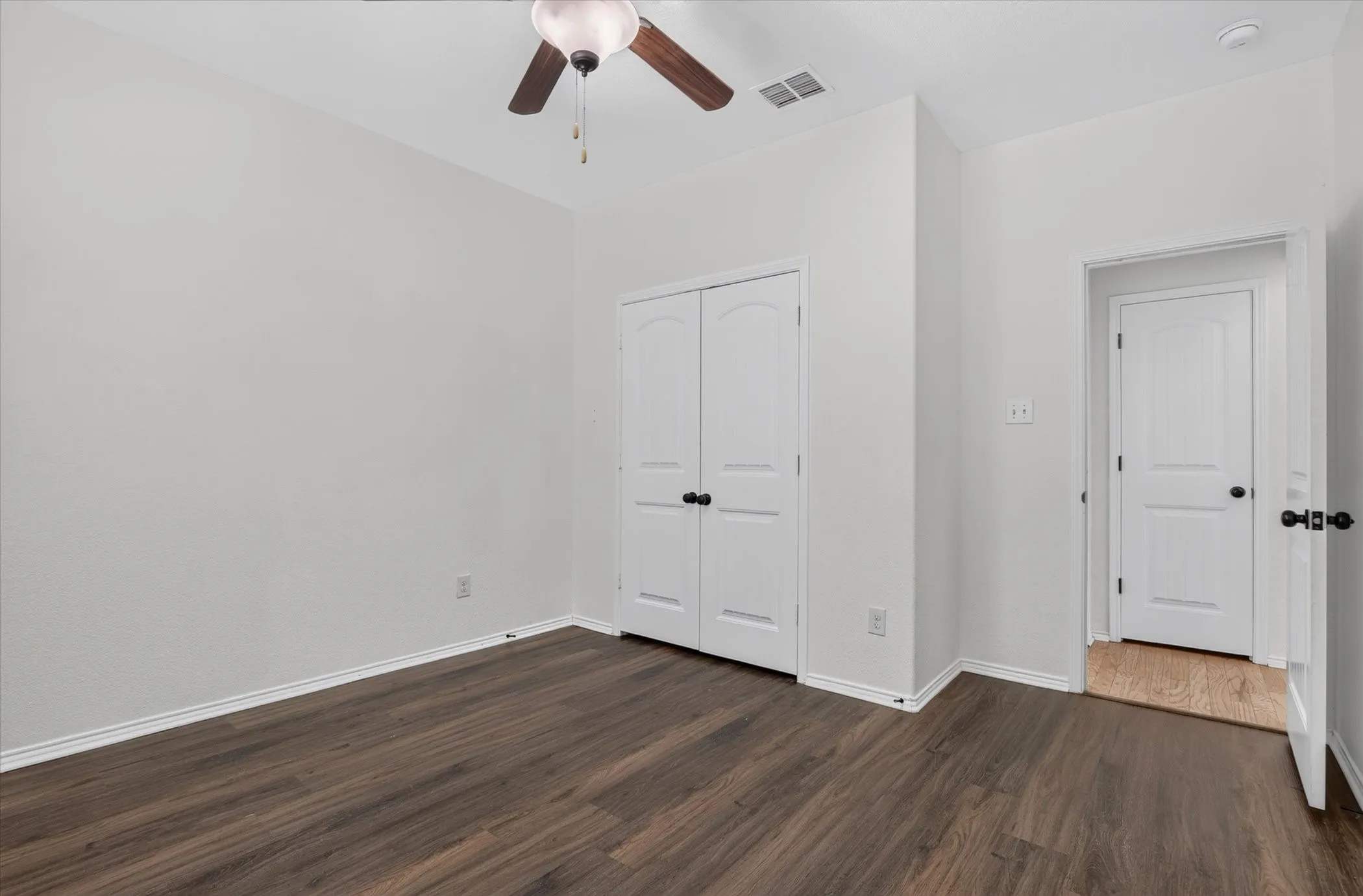 Room featuring wood-finish flooring, white walls, and a ceiling fan