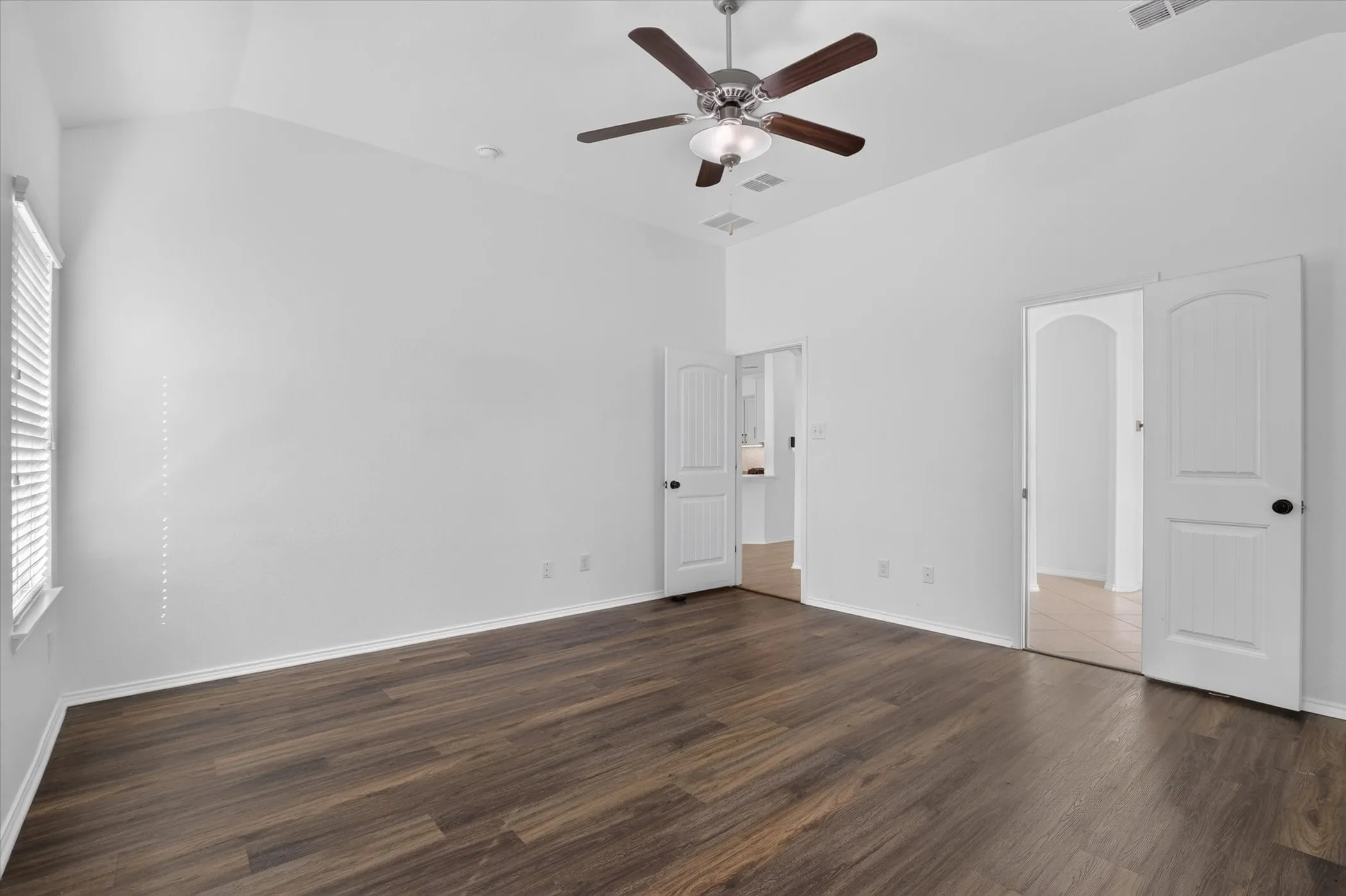 Vaulted ceiling, wood-finish flooring, ceiling fan with integrated lighting, window with blinds, and white interior doors