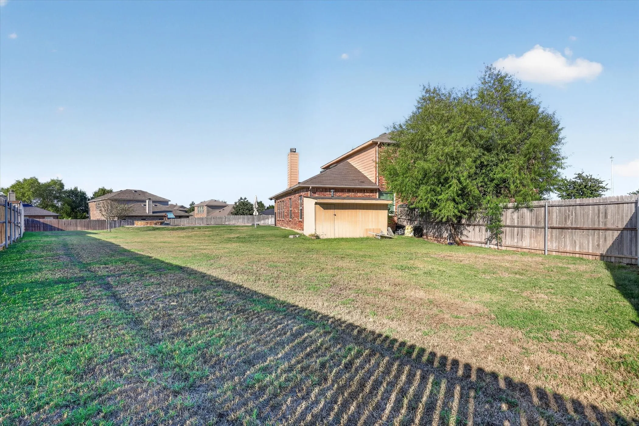 Expansive grassed area featuring a mature tree, wood fencing, and a brick-clad structure with a chimney