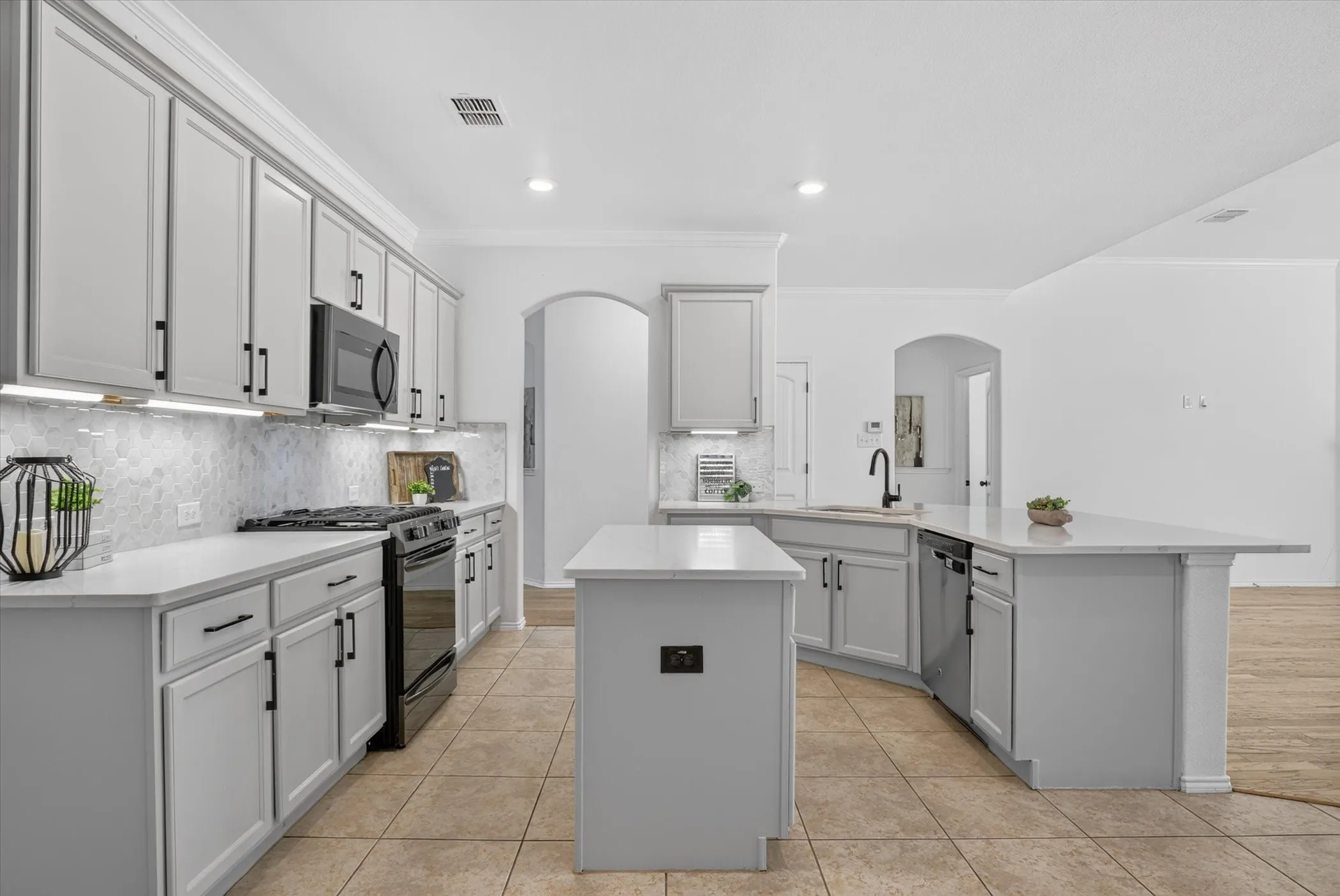 Kitchen featuring light gray cabinetry, white countertops, a mosaic tile backsplash, stainless steel appliances, and a central island with an integrated sink