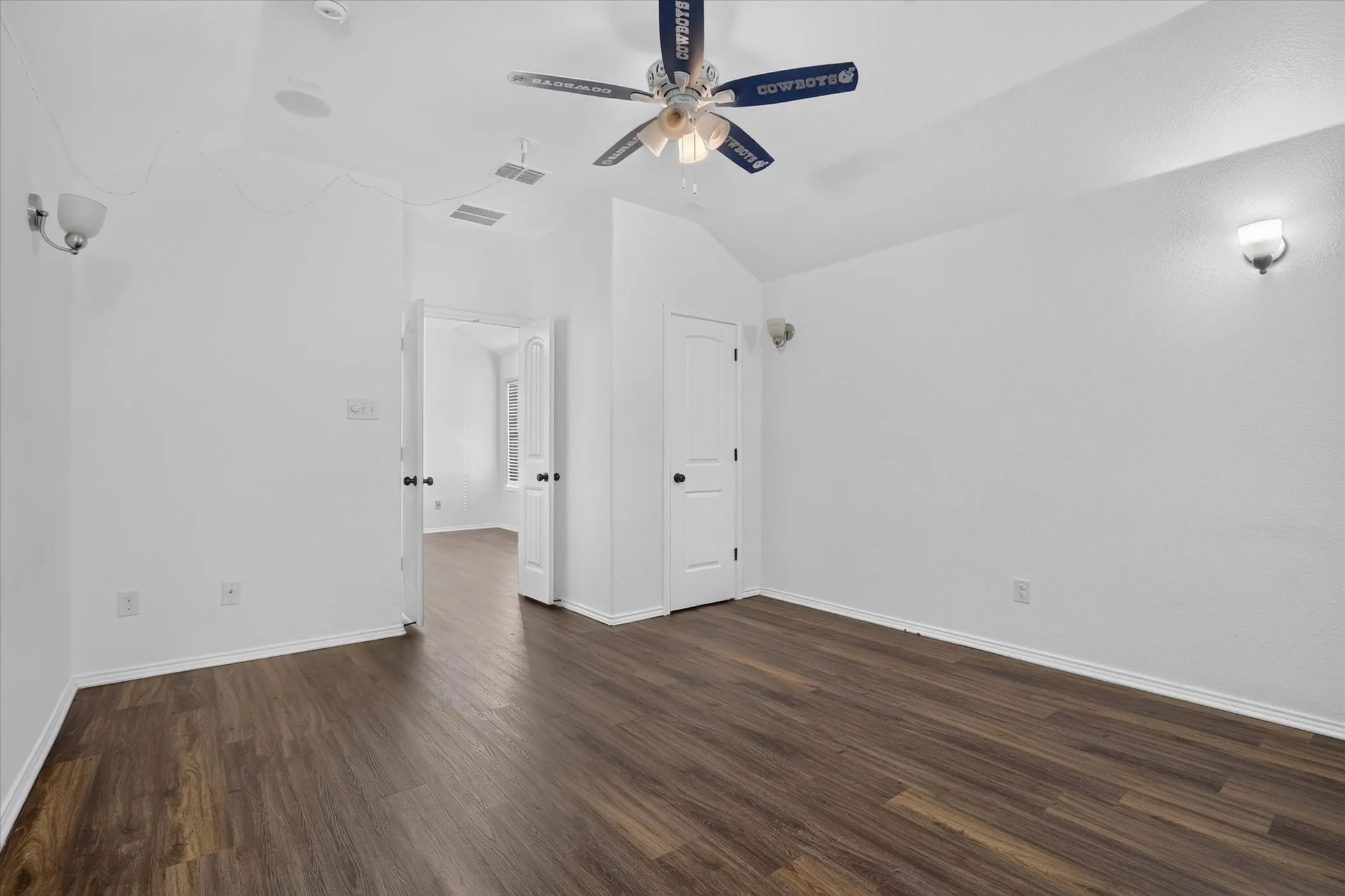 Vaulted ceiling with a ceiling fan, wood-finish flooring, two wall sconces, and interior doors with black hardware