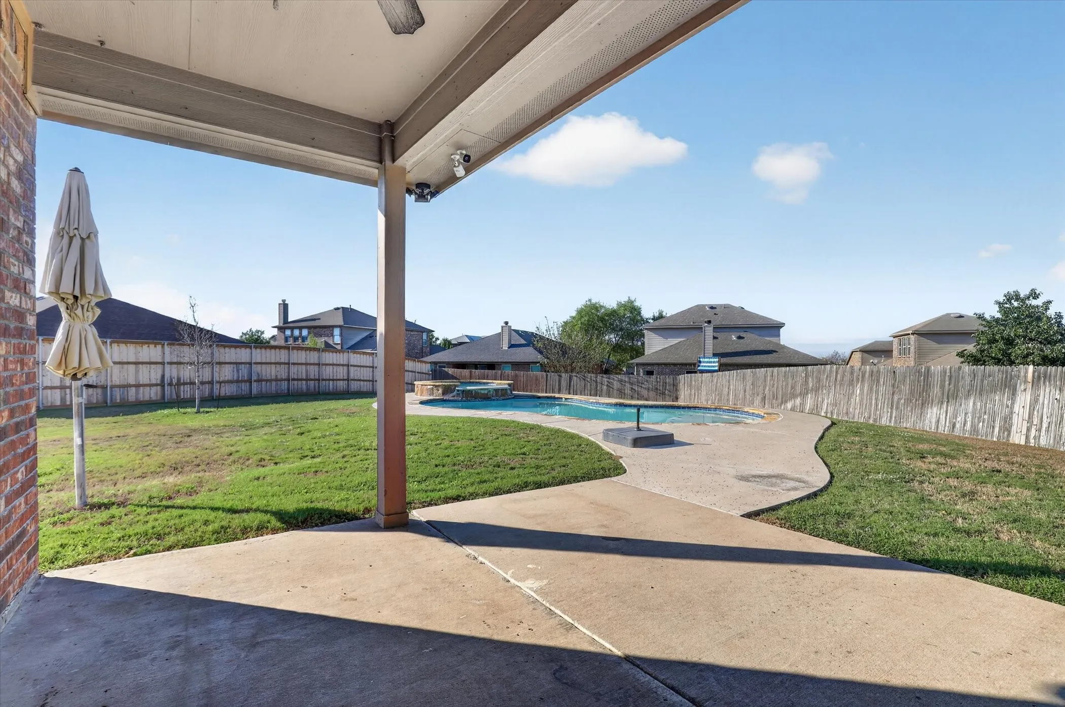 Covered patio with an outdoor ceiling fan, expansive lawn, concrete patio, and a swimming pool