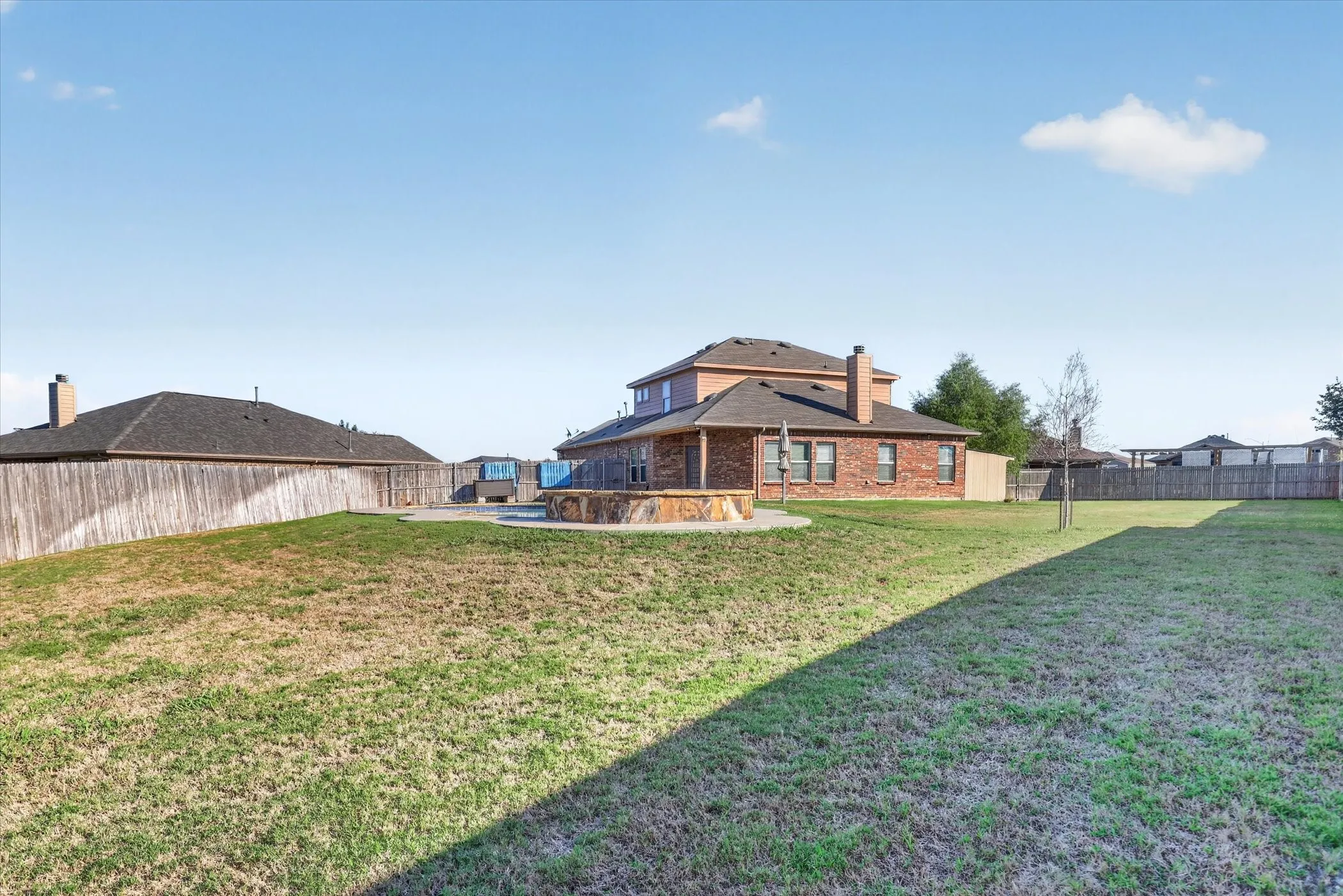 Spacious rural property featuring a brick-constructed residence with blue metal roof accents, positioned on expansive grounds with mature landscaping