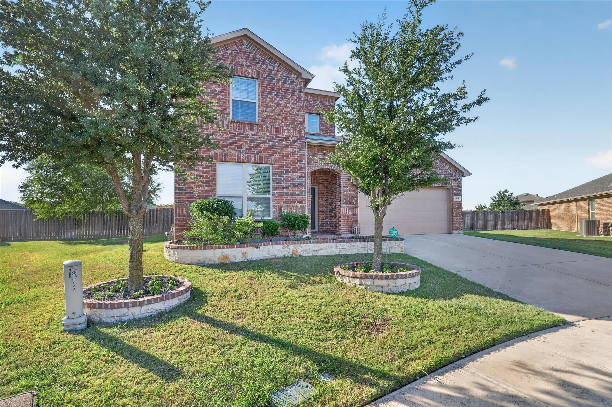 Brick facade, arched entry, two-car garage, concrete driveway, and established landscaping with stone-accented planters