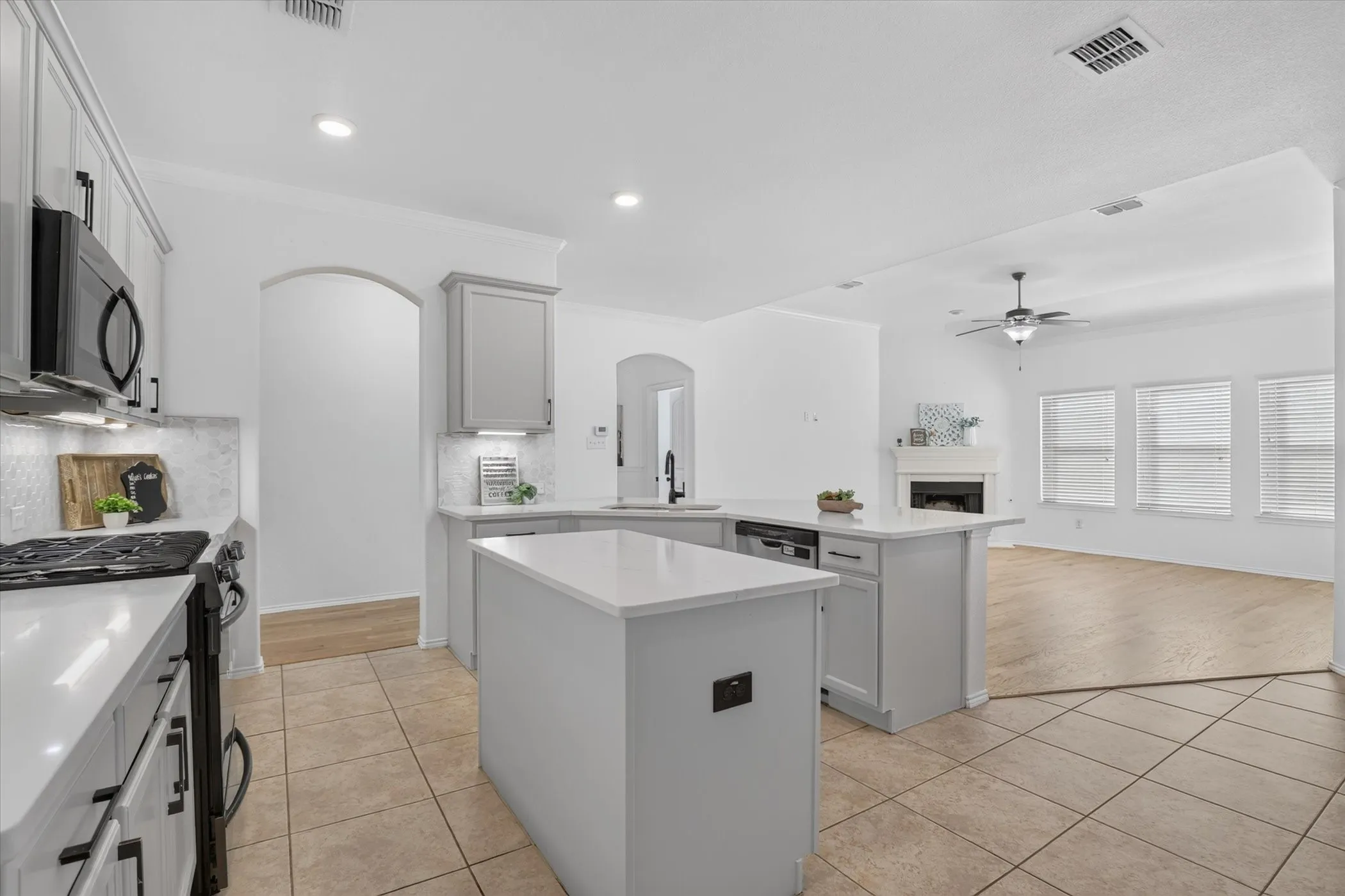 Spacious kitchen featuring a large center island with waterfall countertop, white cabinetry with arched detailing, stainless steel appliances, tile flooring, and abundant natural light from multiple windows