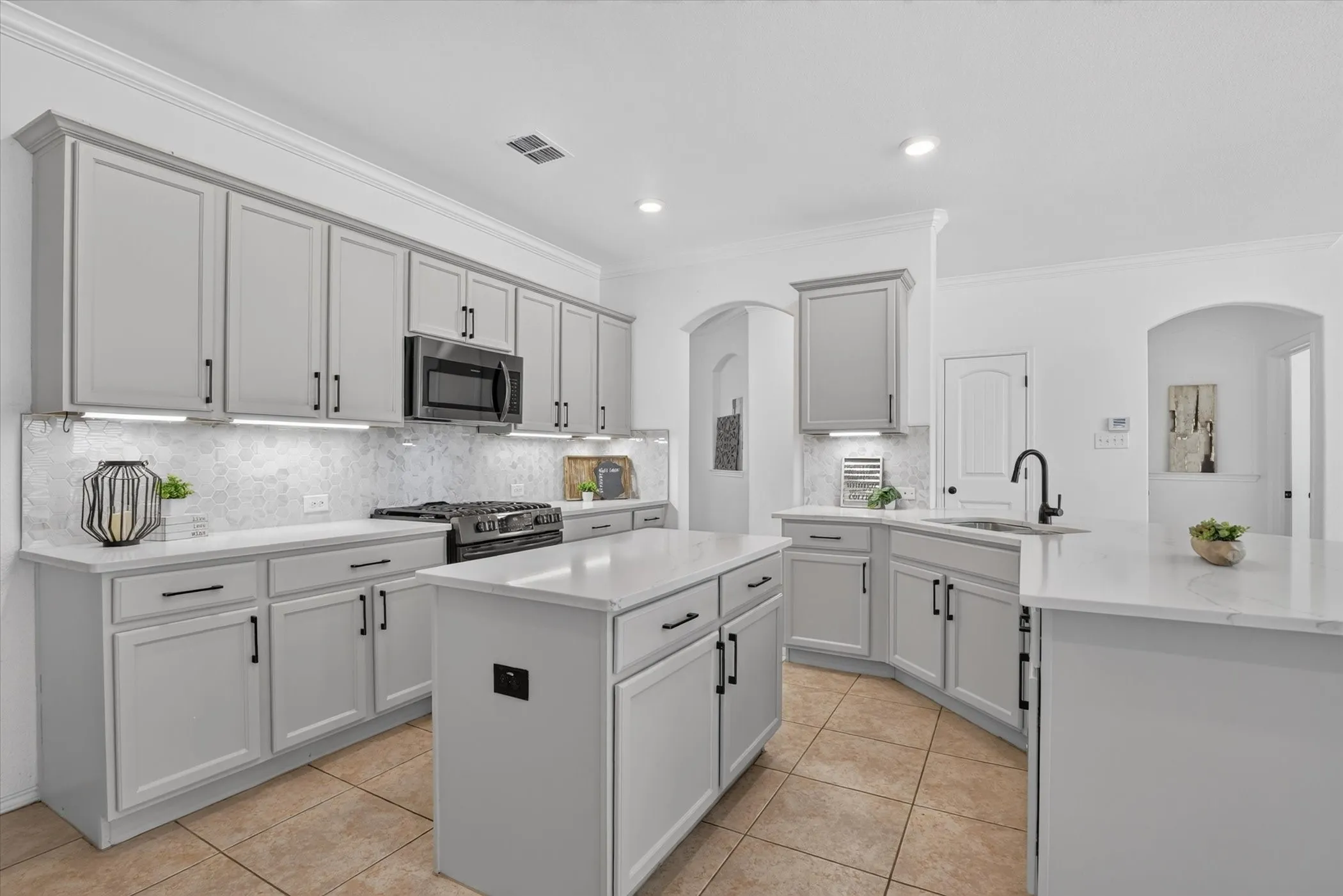 Light gray cabinetry with black hardware, white countertops, tile flooring, recessed lighting, and a built-in microwave