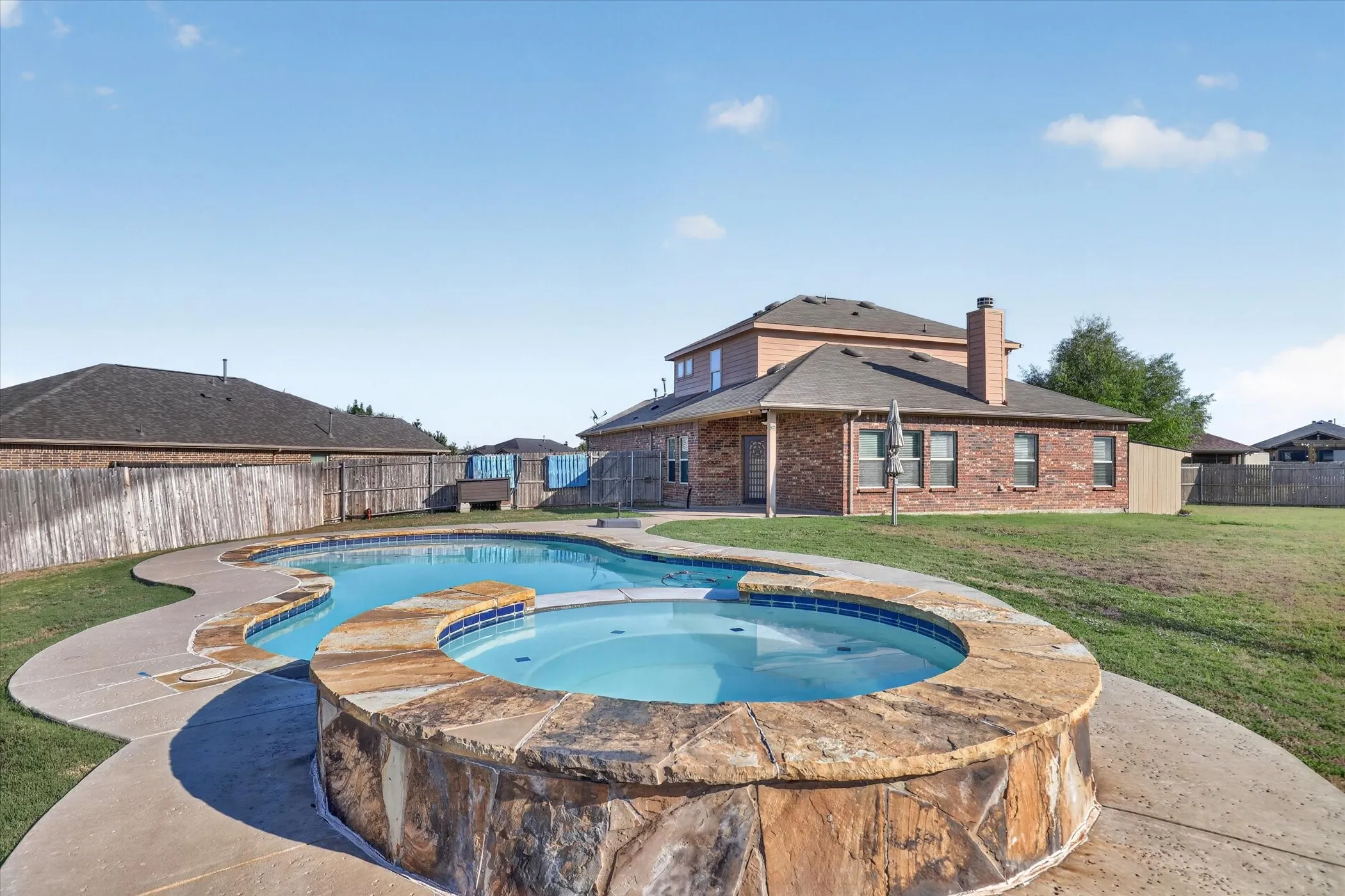 Freeform swimming pool with an integrated spa, stone-clad spa surround, and concrete decking