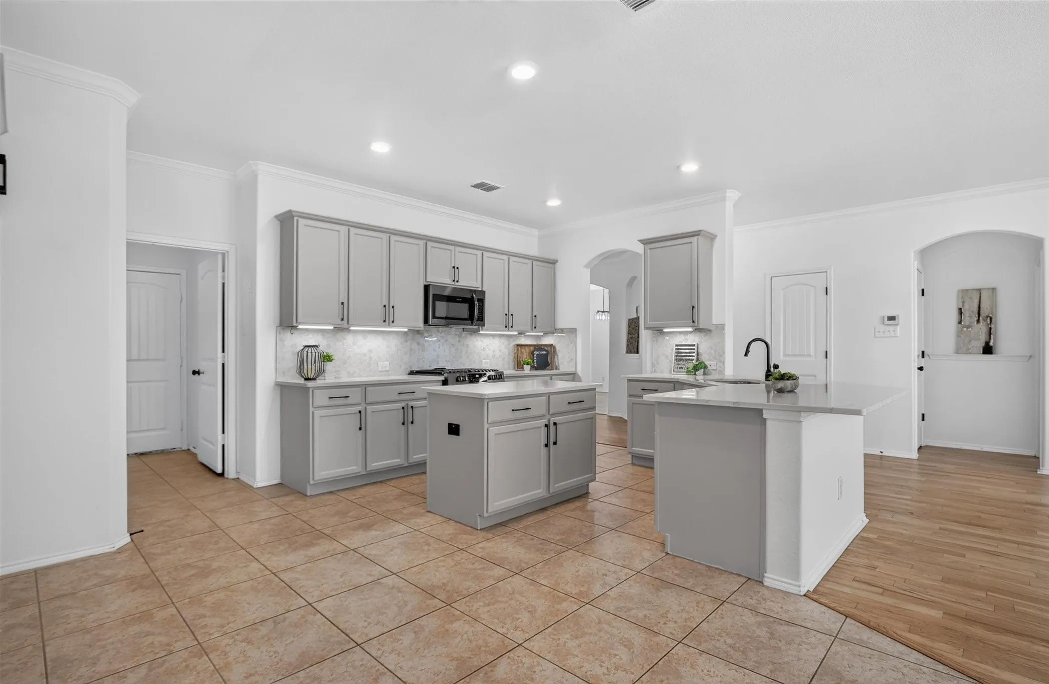 Kitchen featuring light gray cabinetry, a central island with a solid surface countertop, a second island with an integrated sink and faucet, tile flooring, and recessed lighting