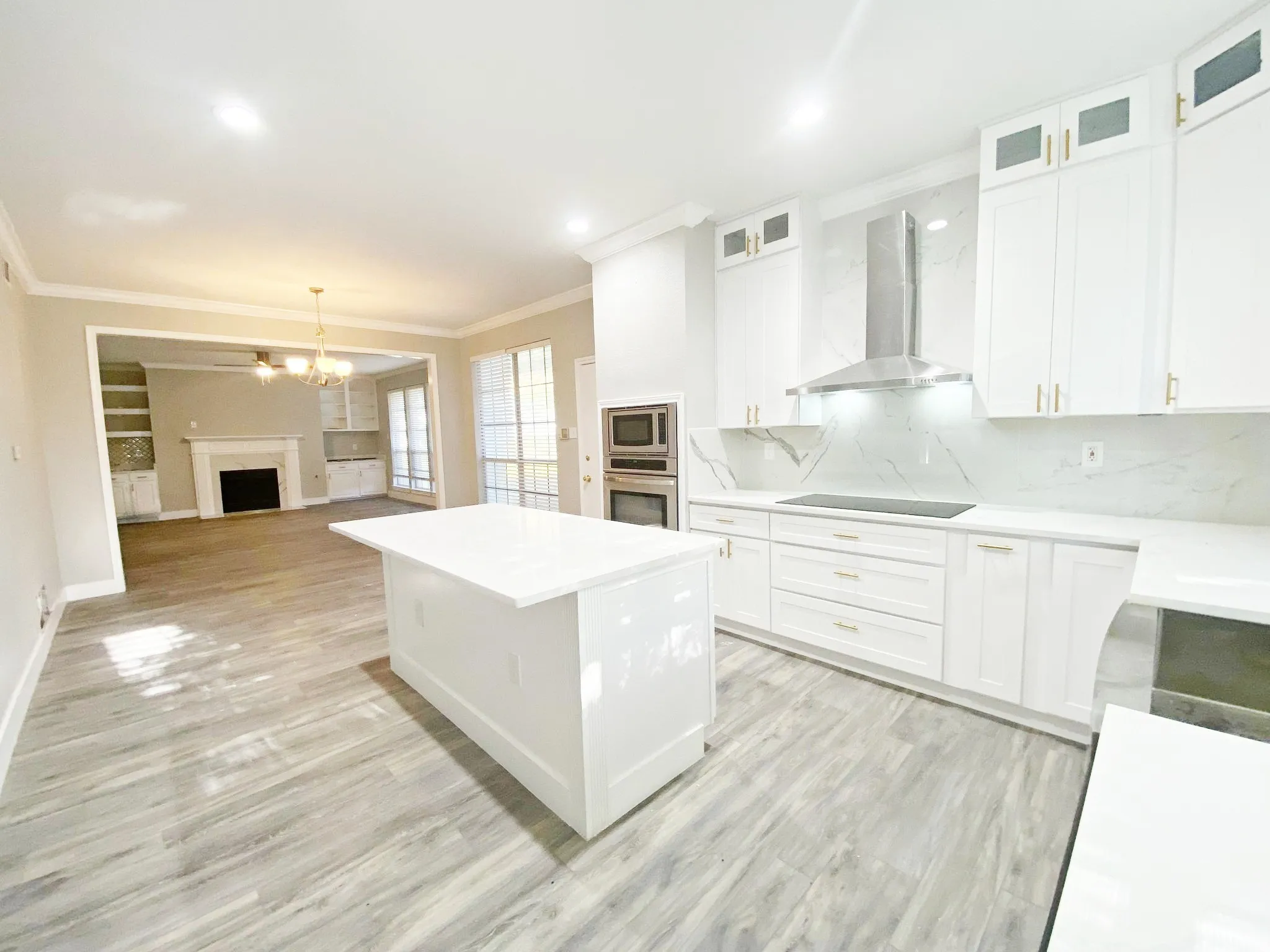 Kitchen featuring backsplash, light hardwood / wood-style flooring, stainless steel appliances, wall chimney range hood, and white cabinetry