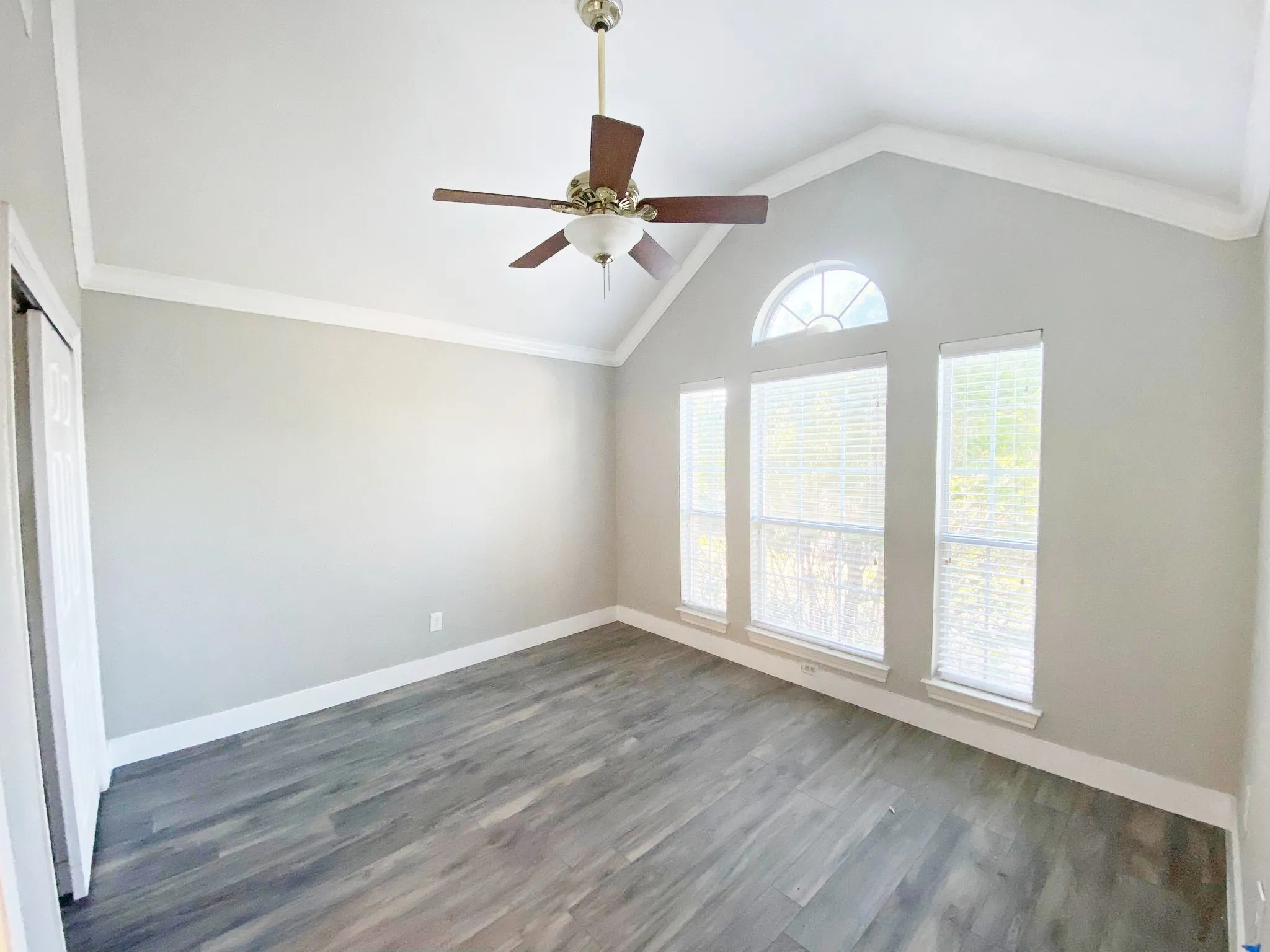 Empty room with crown molding, dark hardwood / wood-style flooring, ceiling fan, and lofted ceiling