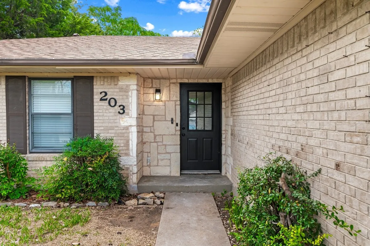 Exterior facade featuring light-toned brick and stone masonry, dark-framed multi-pane front door, and dark shutters