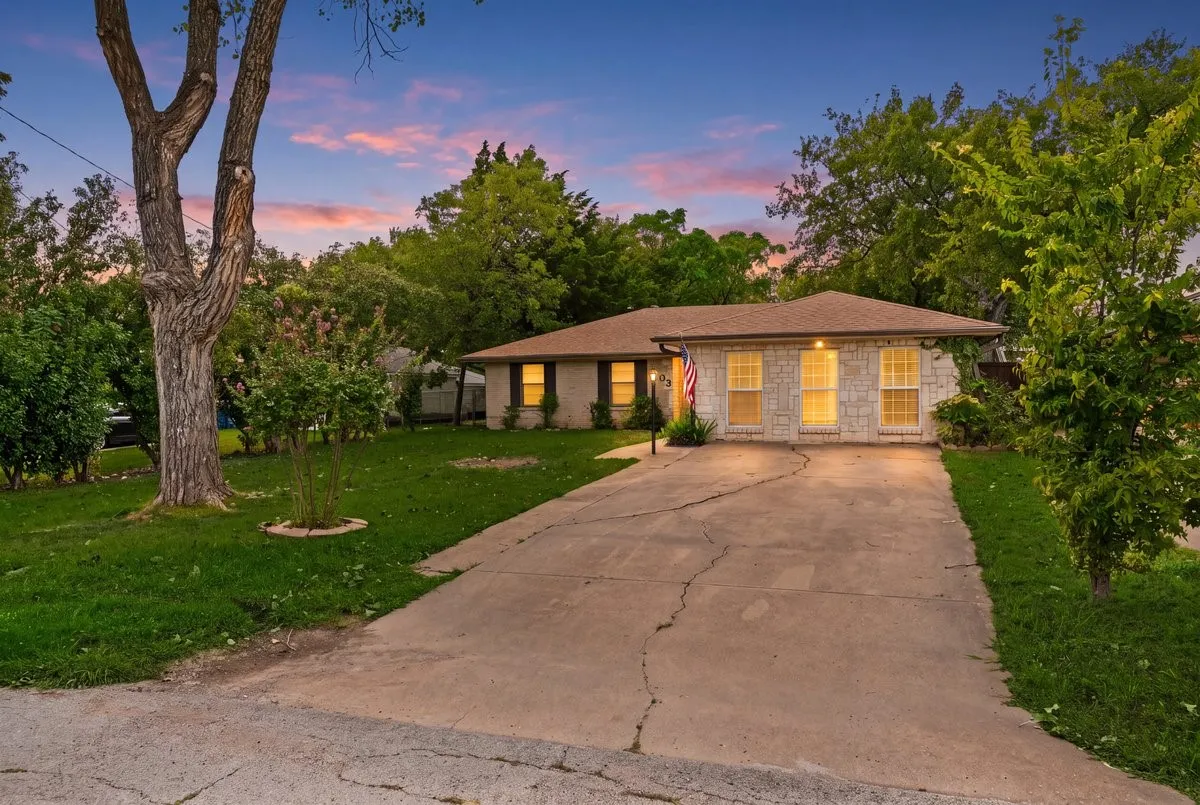 Single-story exterior featuring light-toned stone masonry, a low-pitch roof, symmetrical window placement, and an expansive concrete driveway
