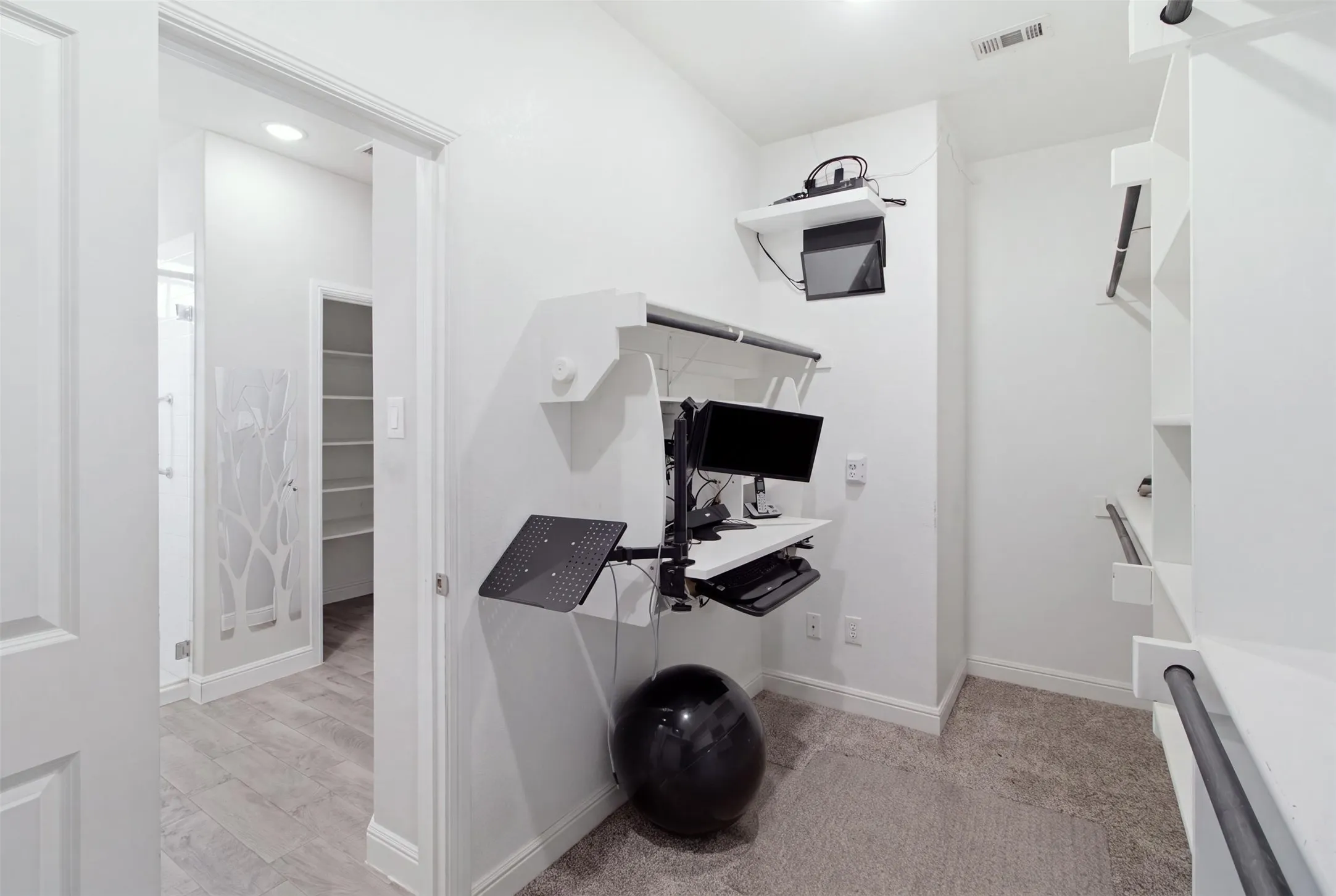 Built-in wall-mounted desk system, custom shelving with hanging rods, recessed lighting, and carpet flooring