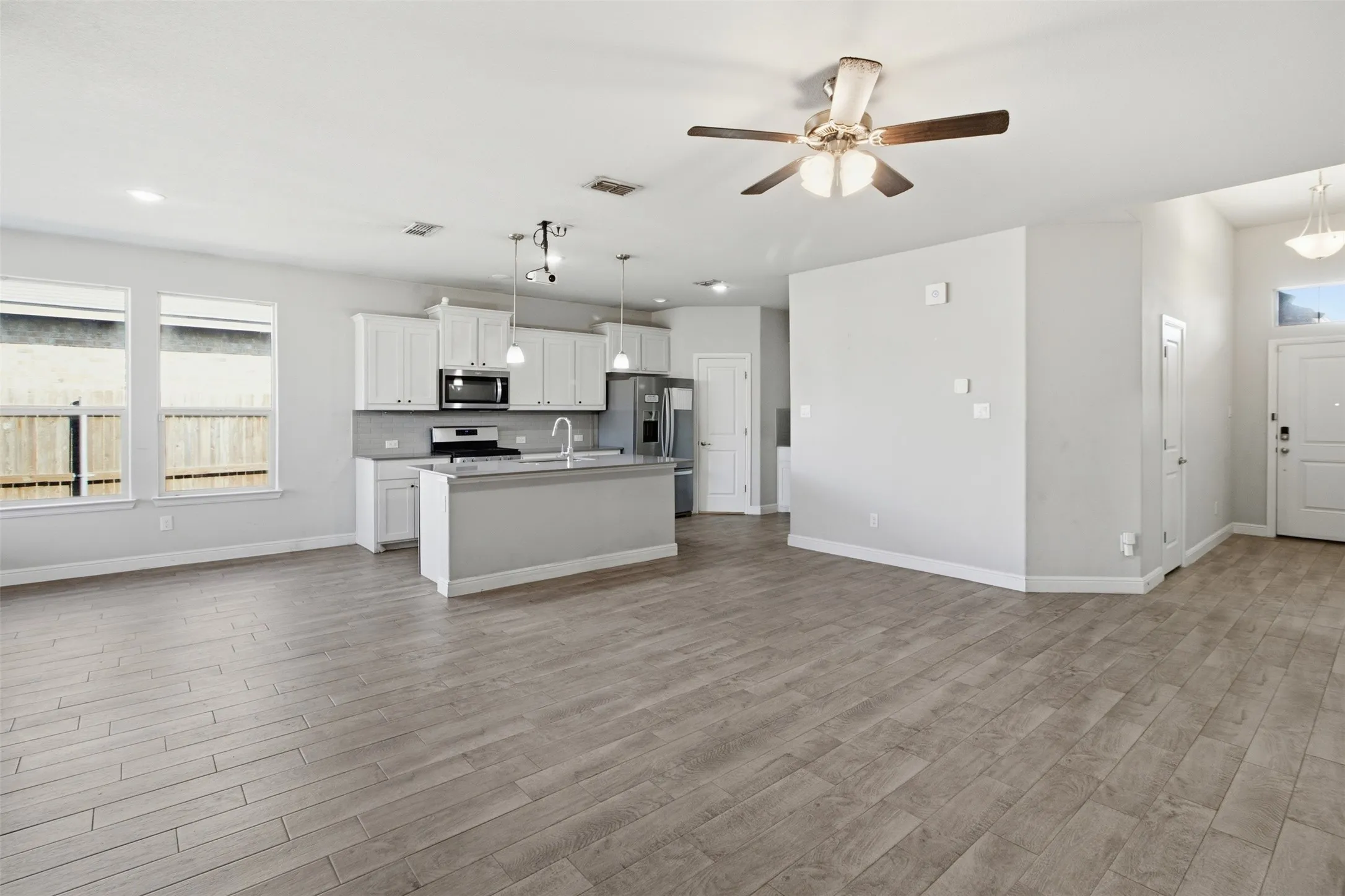 Open-concept living space featuring wood-finish flooring, a contemporary kitchen island, white cabinetry, and stainless steel appliances