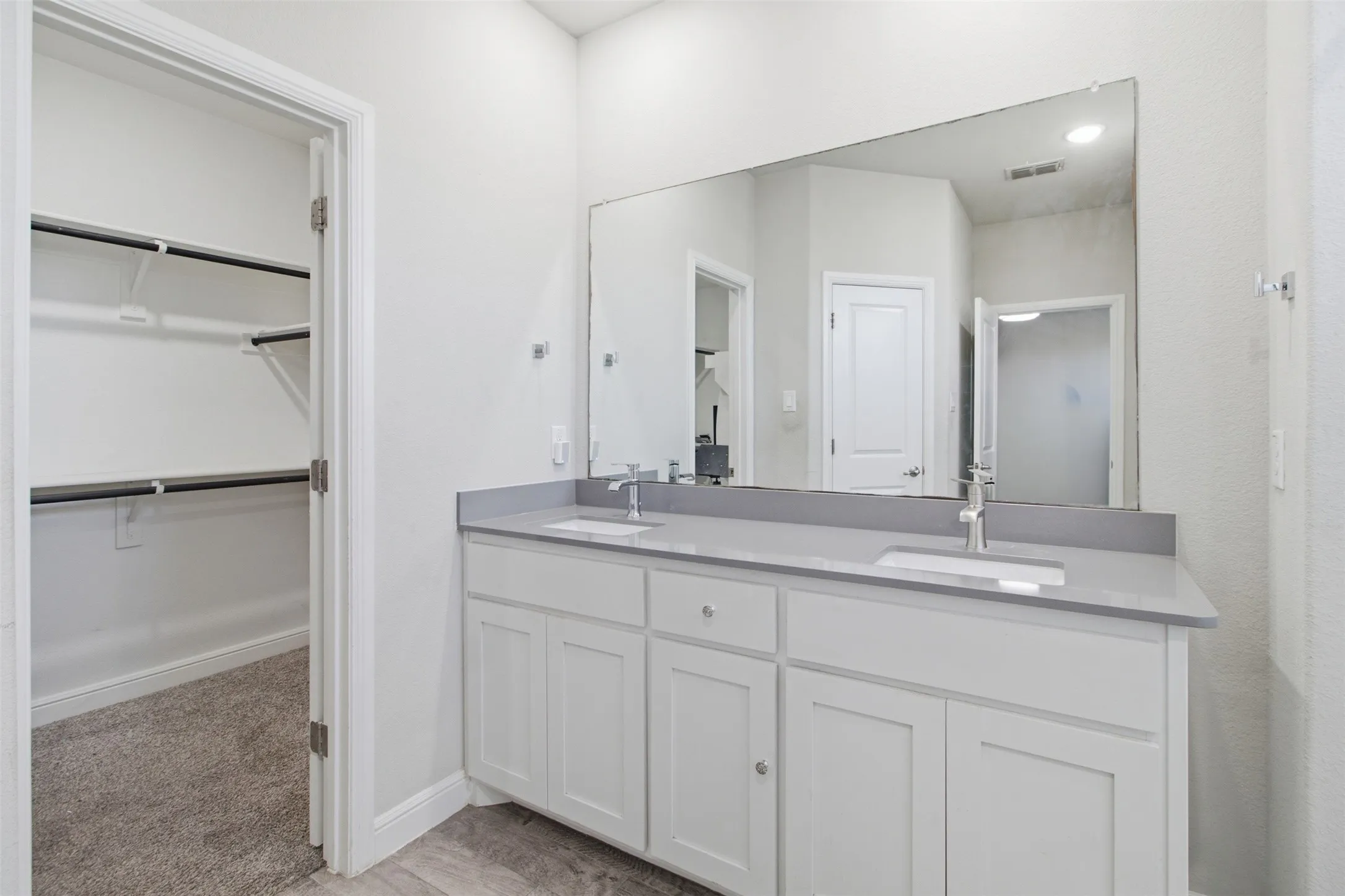 Dual sink vanity with white cabinetry, light gray countertop, and an expansive wall-mounted mirror