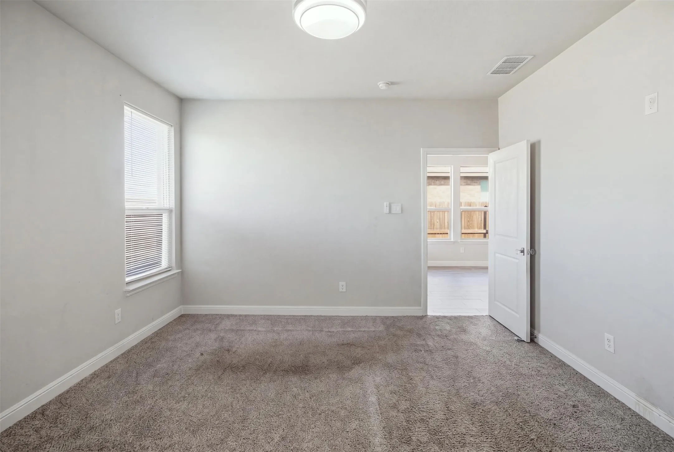Carpeted room with neutral wall tones, a single window with blinds, and a ceiling-mounted light fixture