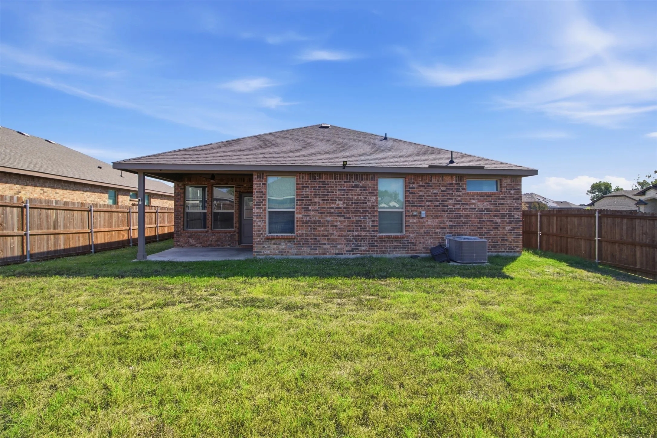 Expansive backyard featuring a covered patio, brick exterior, wood fence, and a pitched roof