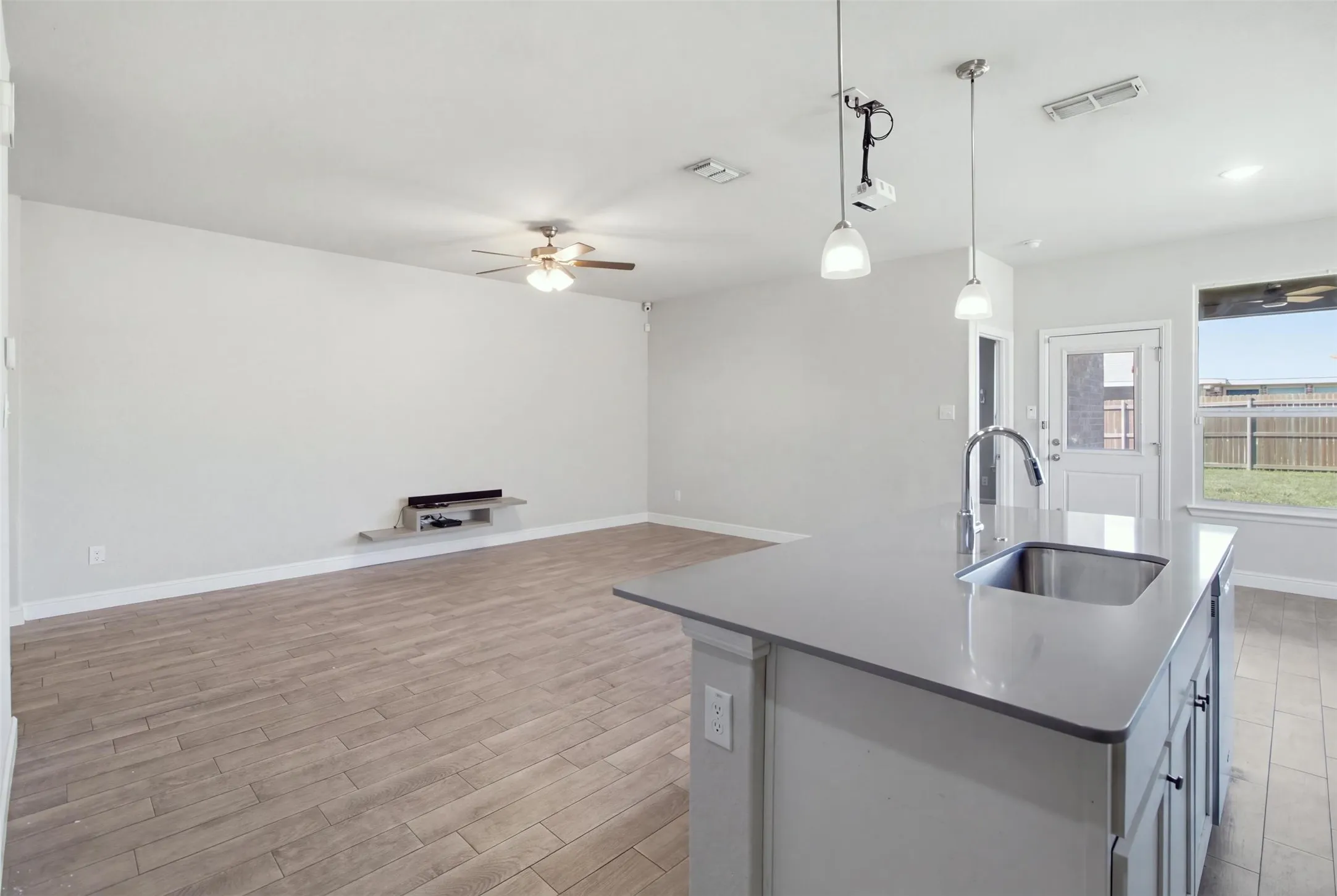 Open-concept living space featuring wood-finish flooring, a ceiling fan, and an island with an undermount sink, gooseneck faucet, and pendant lighting