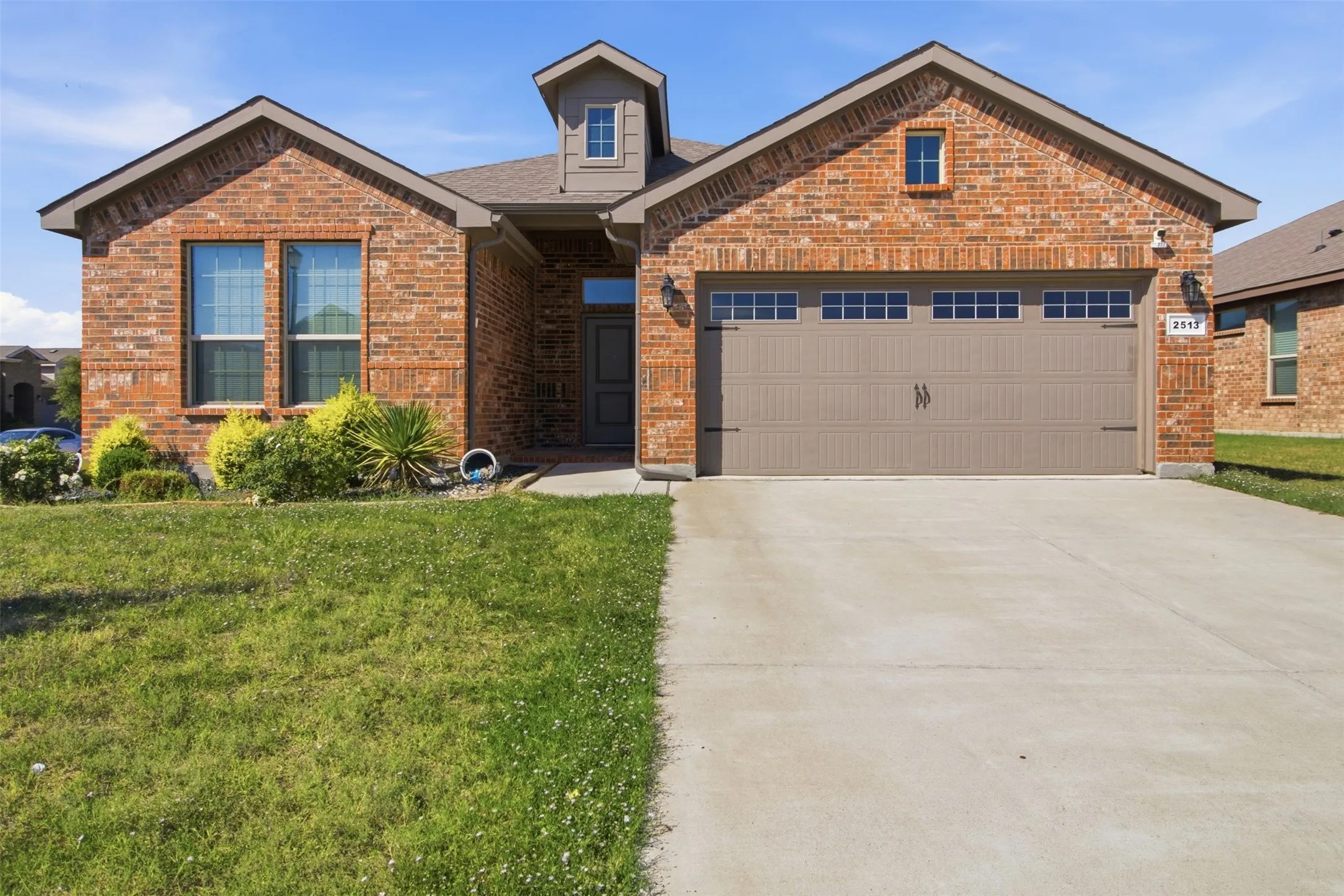 Brick facade with decorative shutters, integrated garage with transom windows, covered entryway, and front landscaping