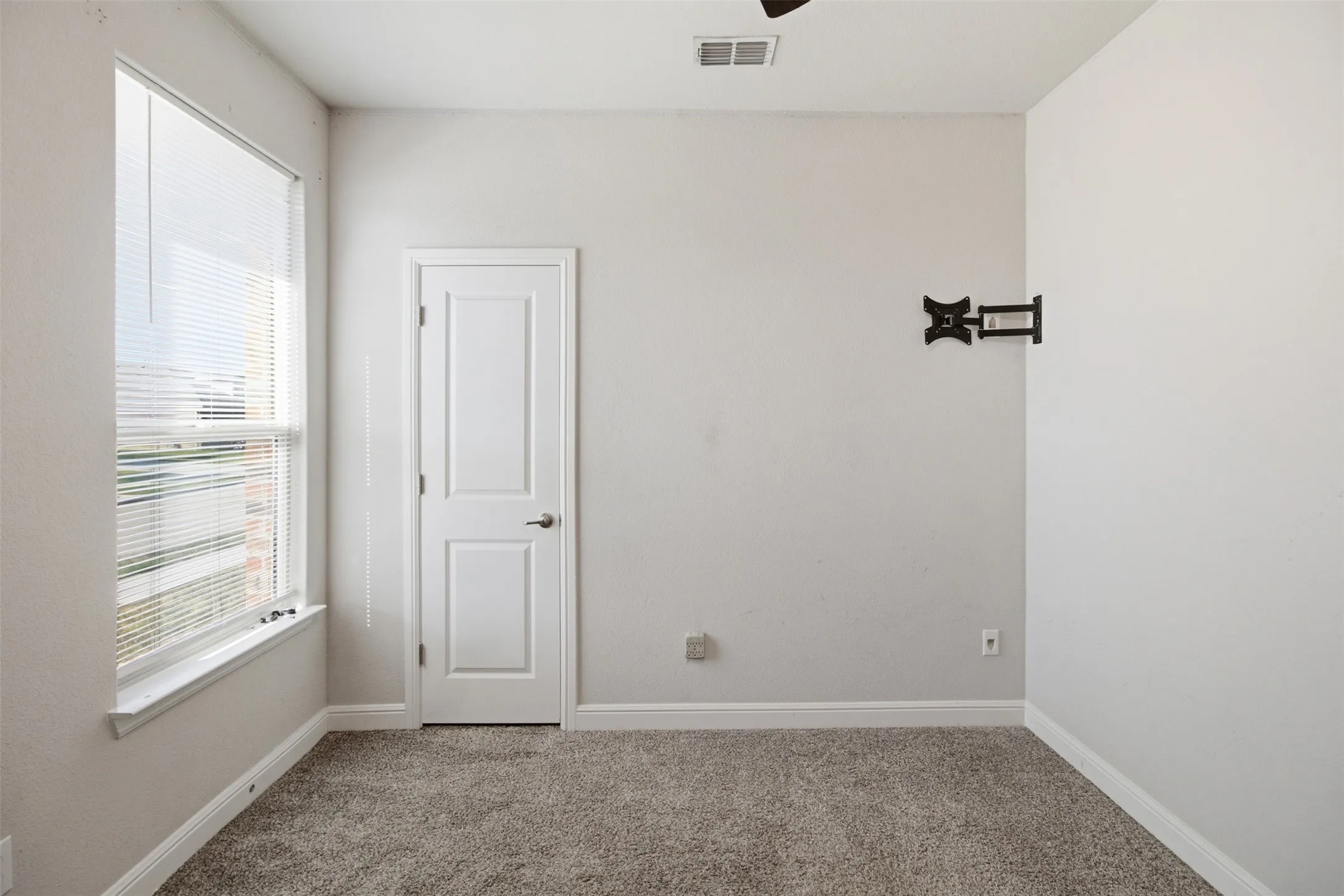 Wall-mounted television bracket, carpet flooring, and a single paneled door