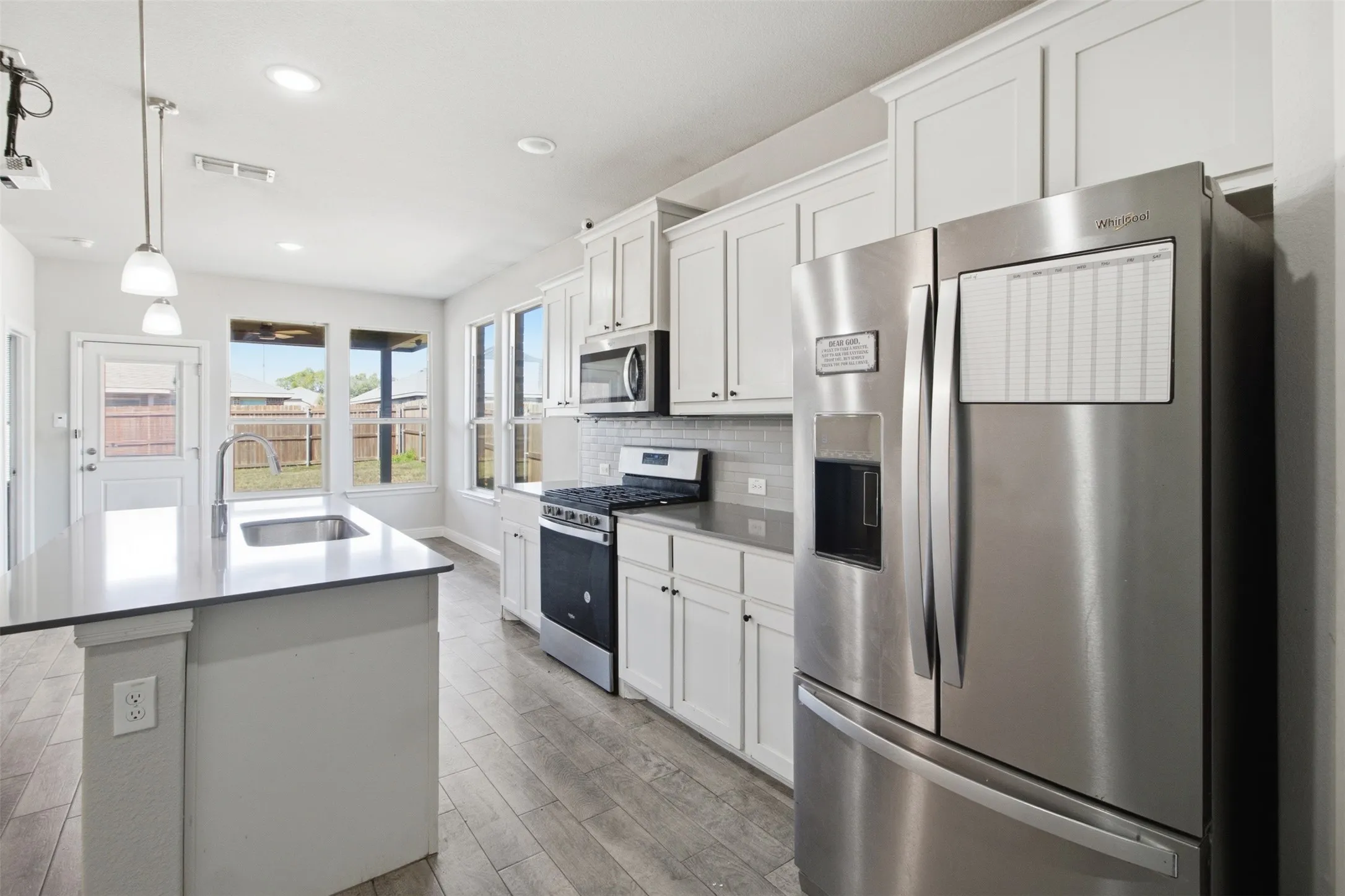 Kitchen featuring white cabinetry, stainless steel appliances, a center island with sink, grey countertops, and wood-finish flooring