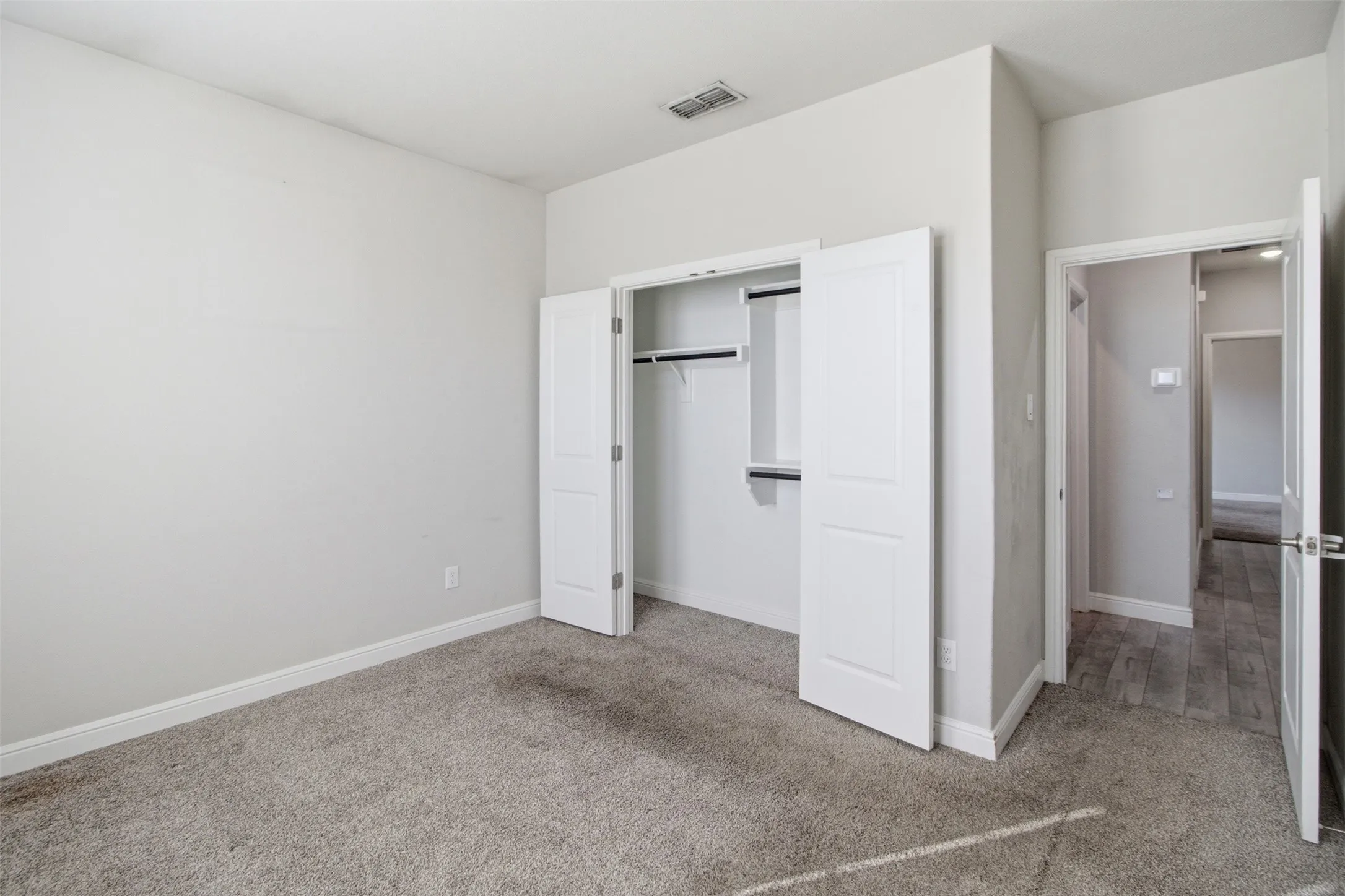 Spacious primary bedroom featuring neutral wall finishes, carpeted flooring, and dual closets with white frame doors and interior shelving