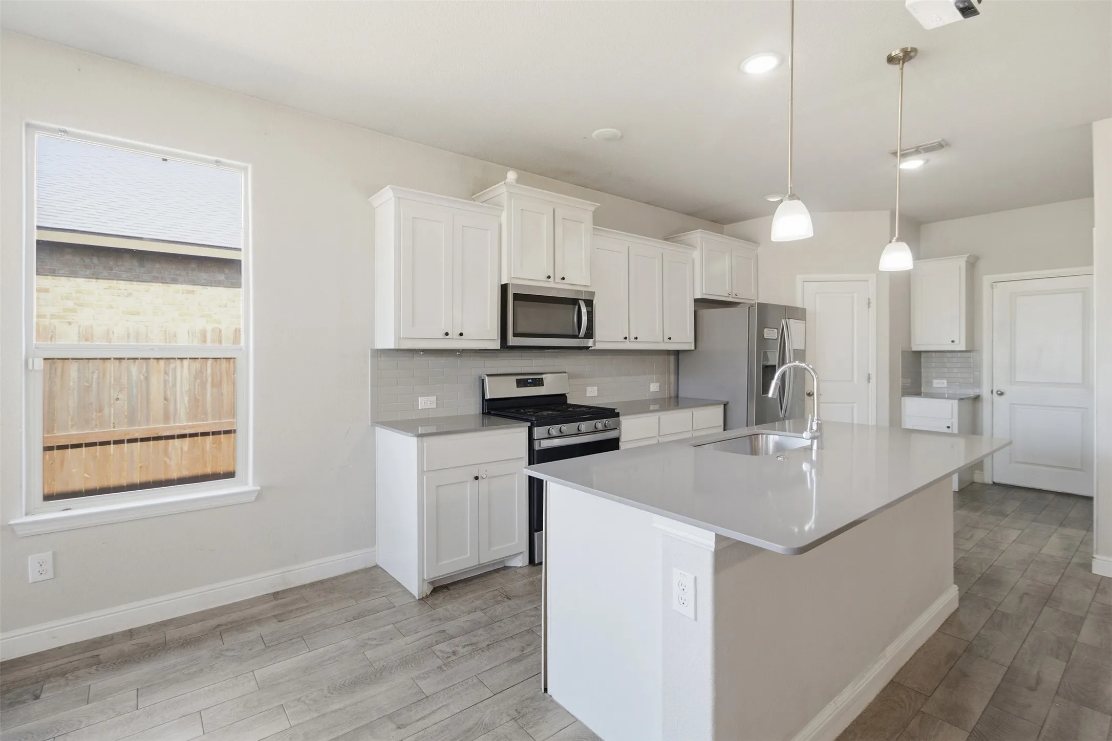 Kitchen featuring white cabinetry, stainless steel appliances, a center island with sink, pendant lighting, and wood-finish flooring