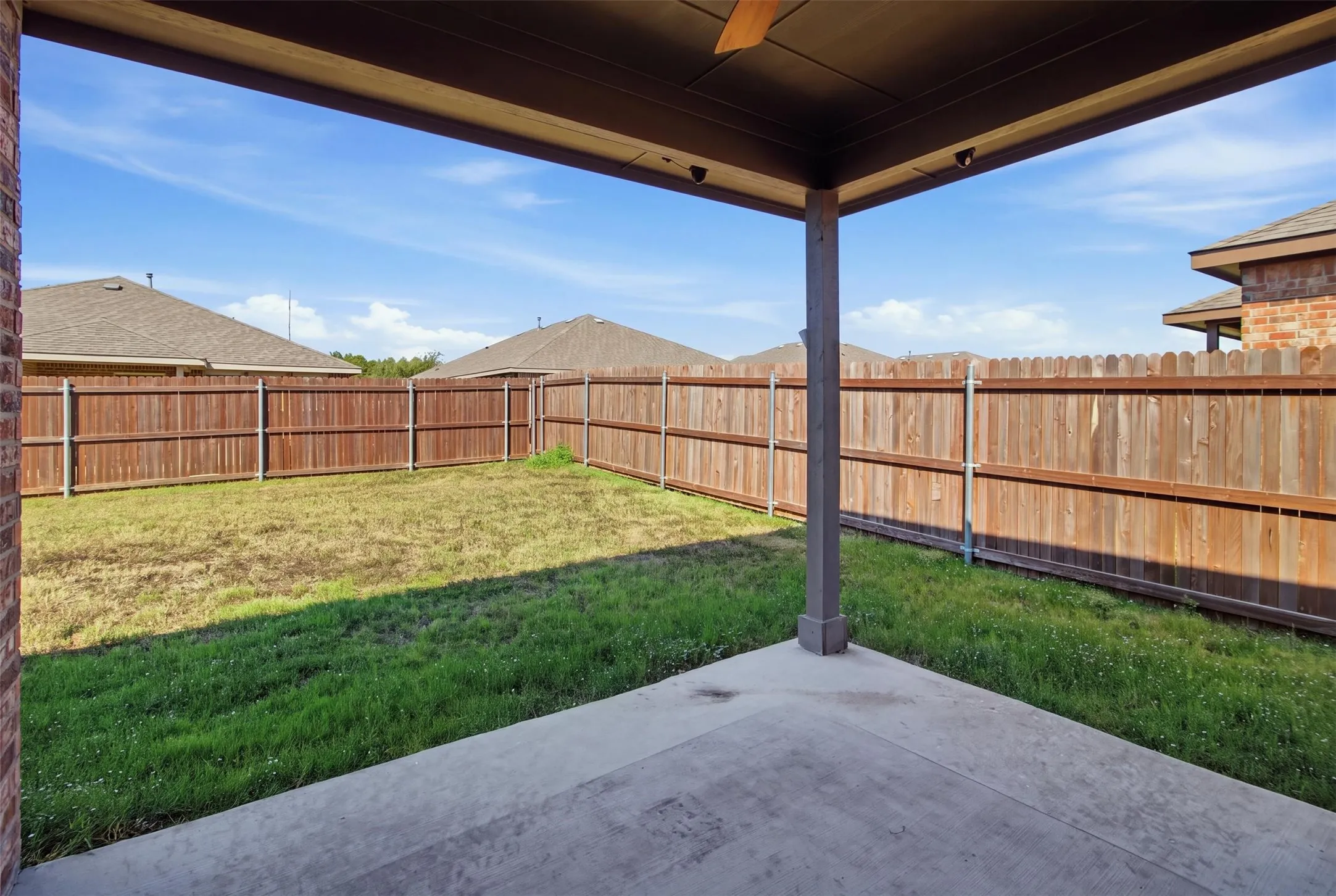 Covered patio with concrete flooring, wood fence enclosure, and a grass lawn area