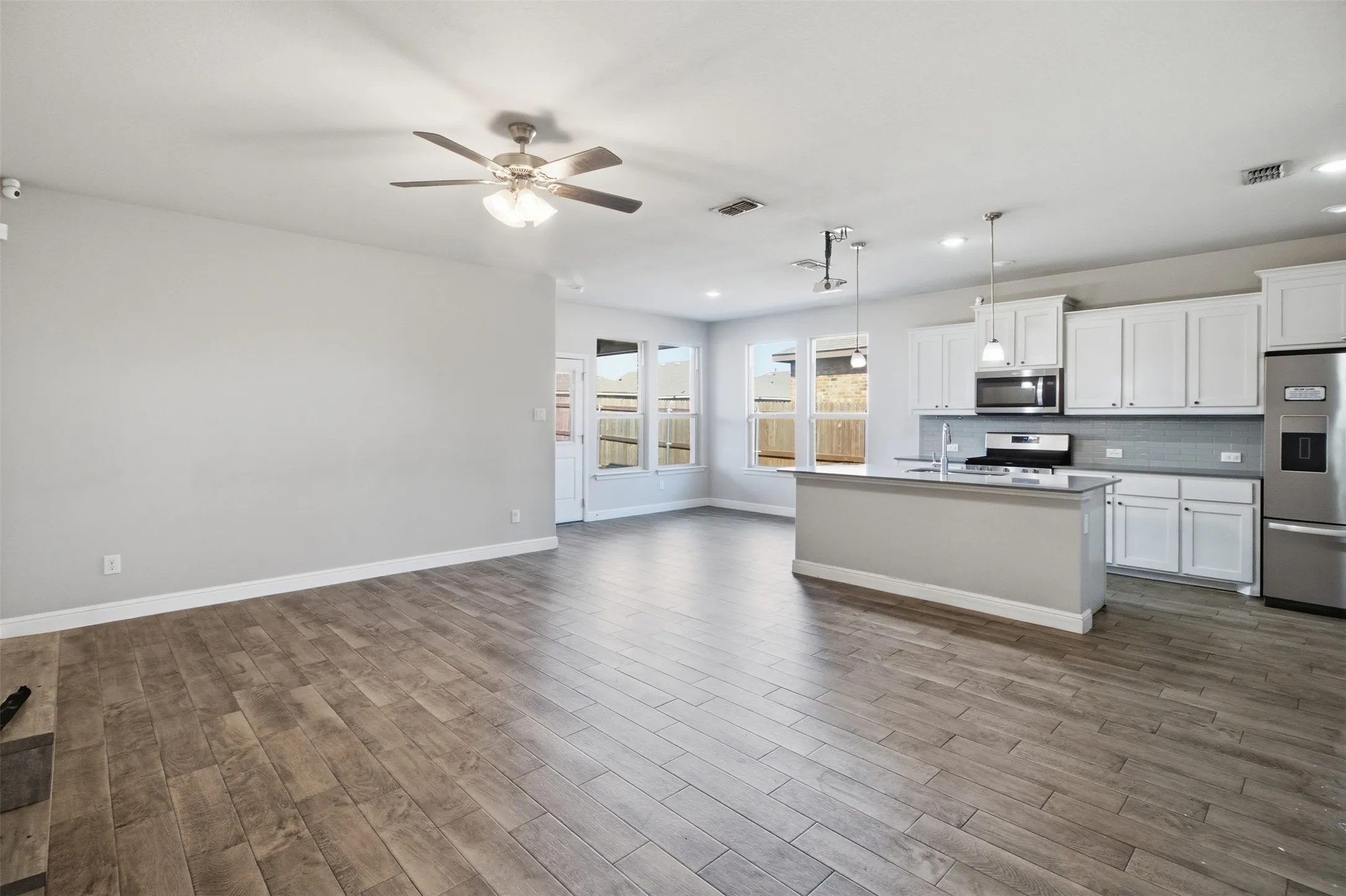 Open-concept living area featuring wood-finish flooring, a contemporary kitchen island, white cabinetry, stainless steel appliances, and a ceiling fan