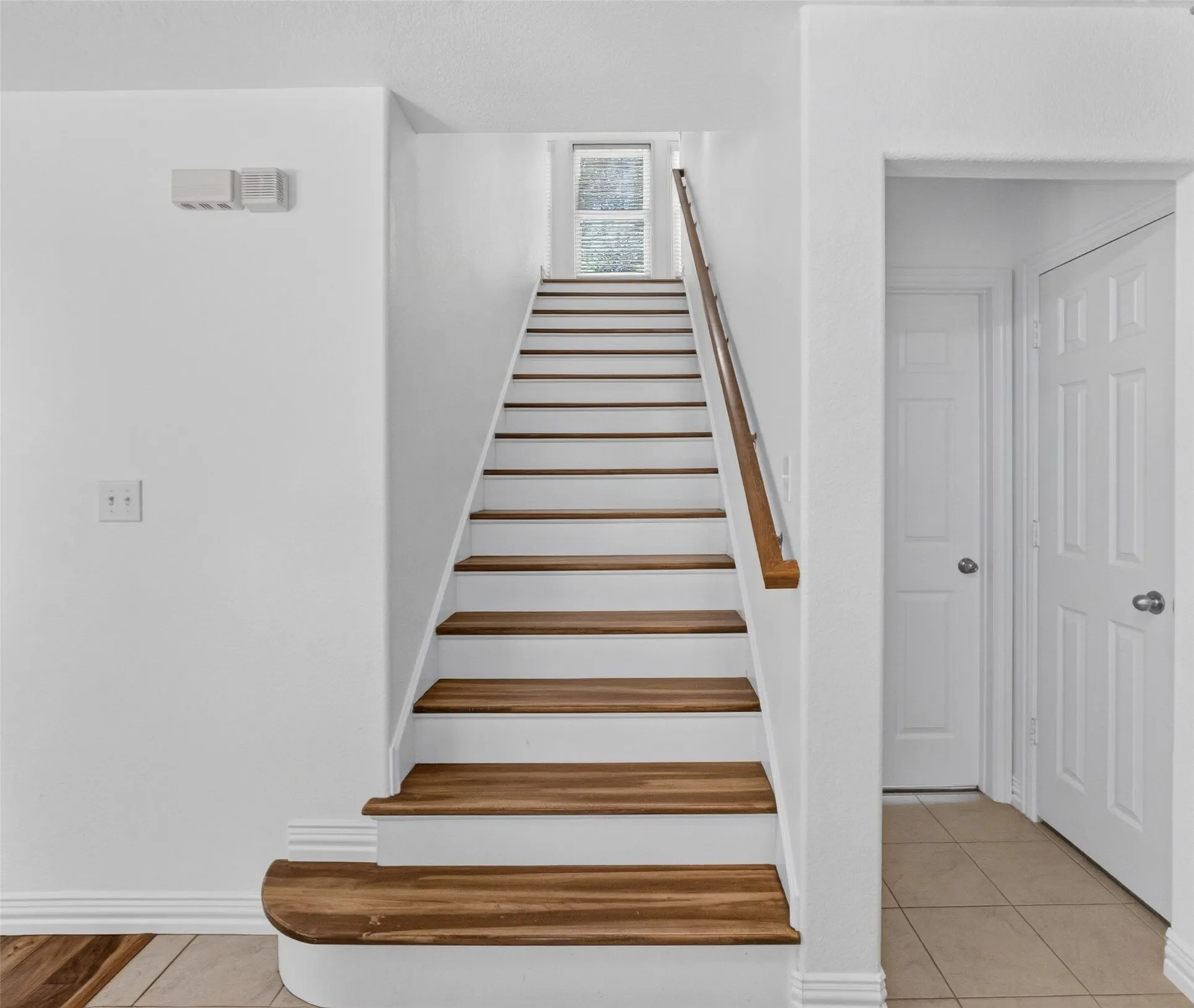 Staircase with wood-finish treads and risers, featuring a wood-finish handrail and a window at the landing