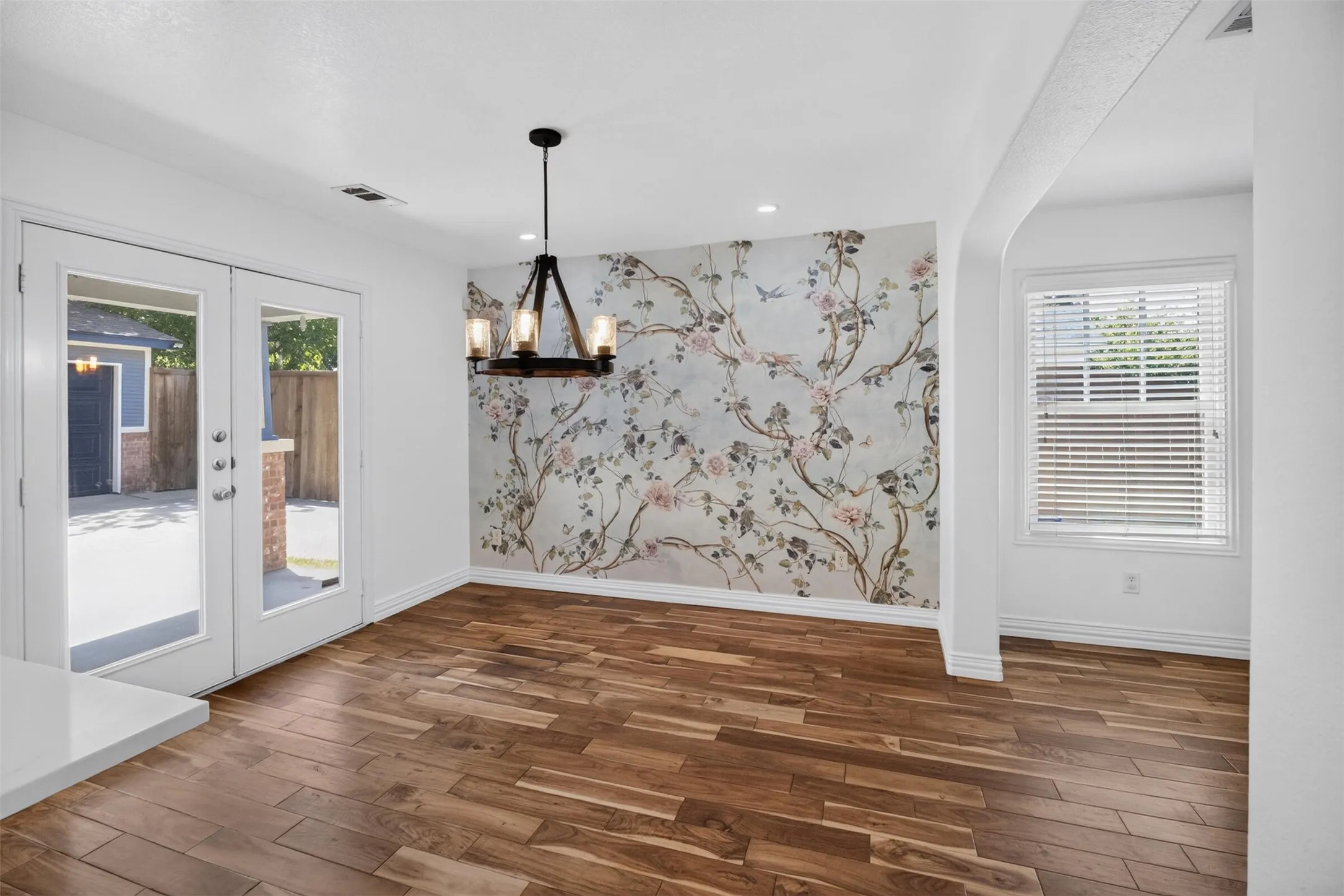 Wood-finish flooring, accent wall with a floral pattern, recessed lighting, double glass-paneled doors, and a decorative chandelier