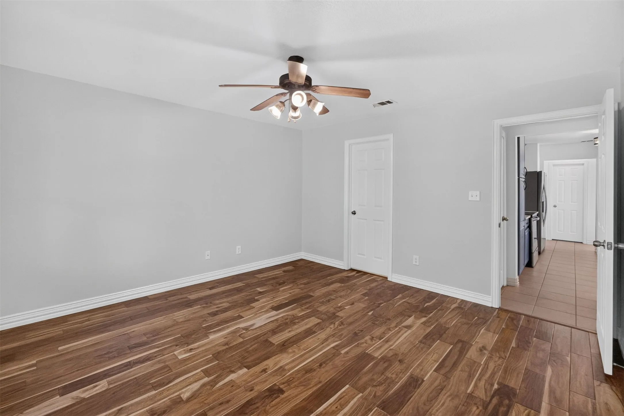 Wood-finish flooring, light grey walls, white trim, and a ceiling fan with integrated lighting