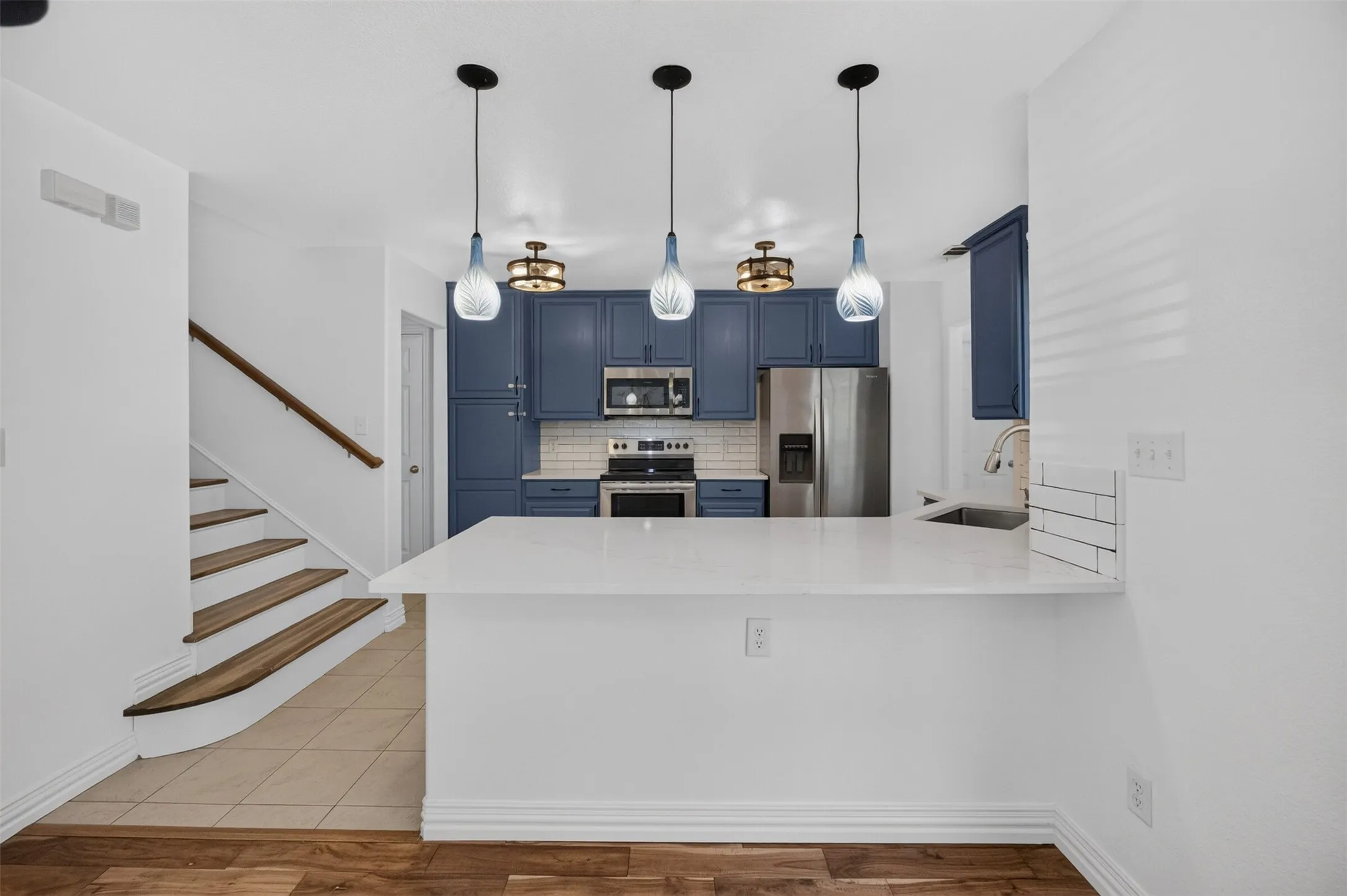 Kitchen with blue cabinetry, stainless steel appliances, white subway tile backsplash, and a white countertop