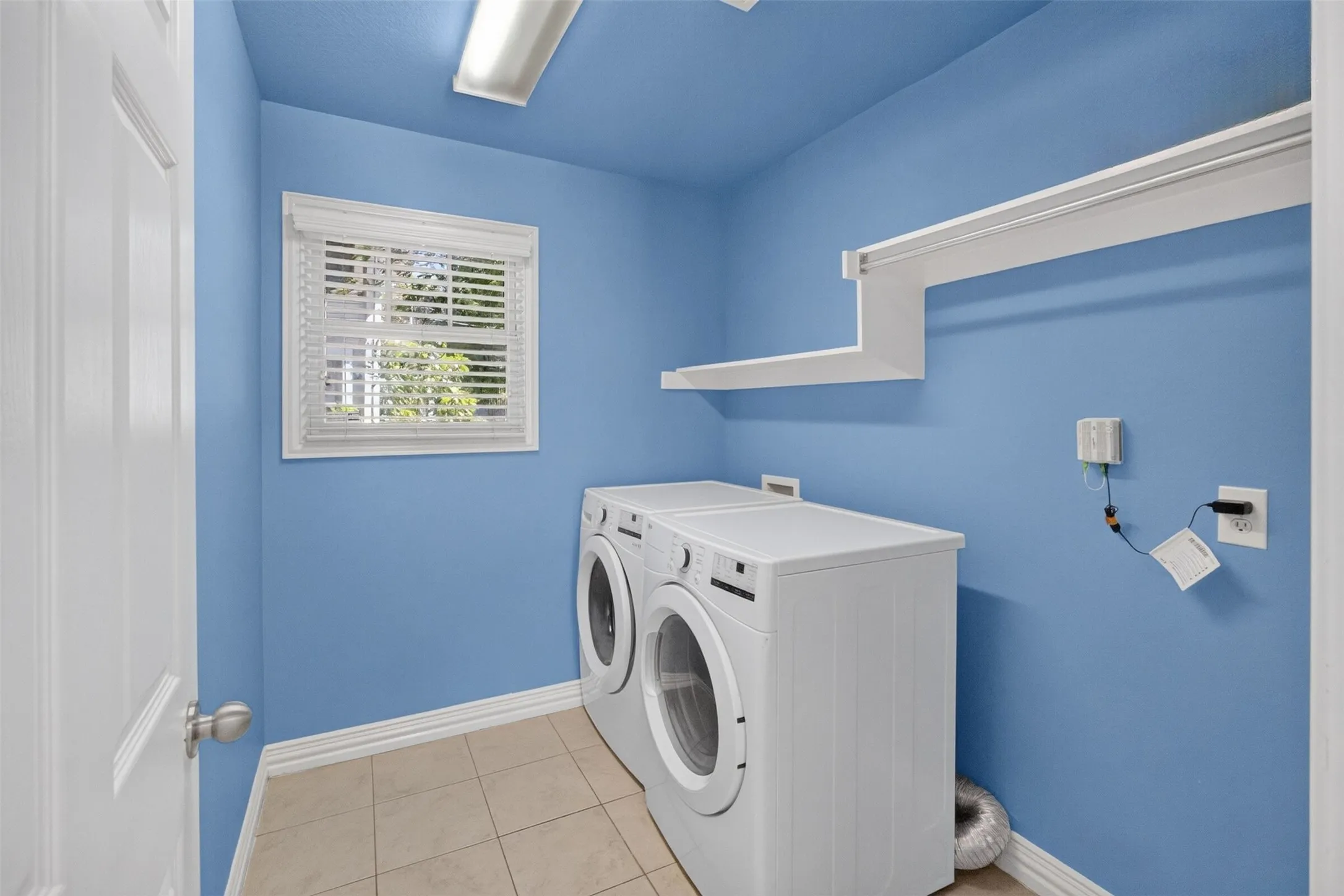 Laundry area featuring a window with blinds, tile flooring, and integrated shelving with a hanging rod