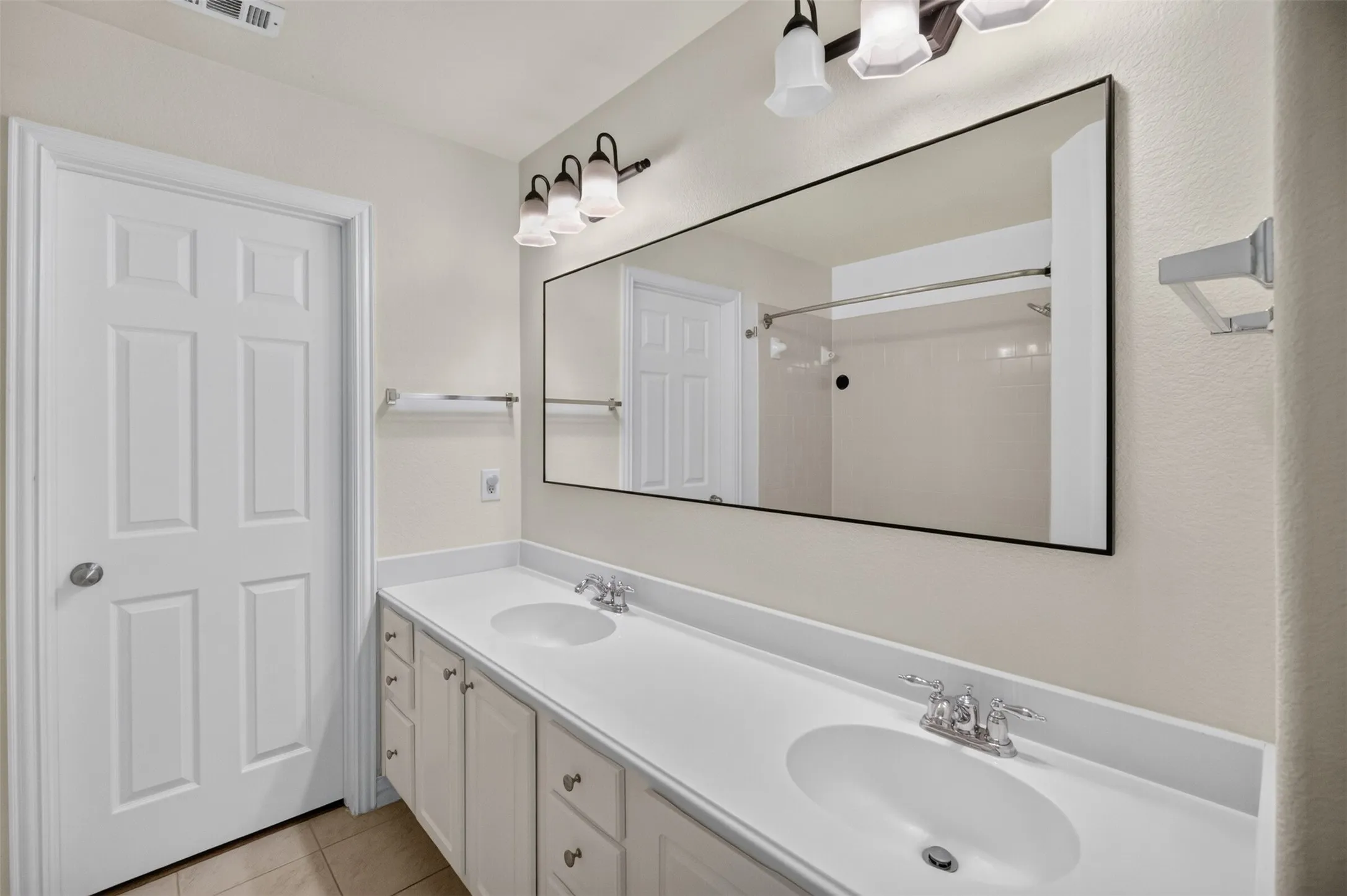 Dual vanity with integrated sinks, white cabinetry, chrome fixtures, a full-width mirror, and tile flooring