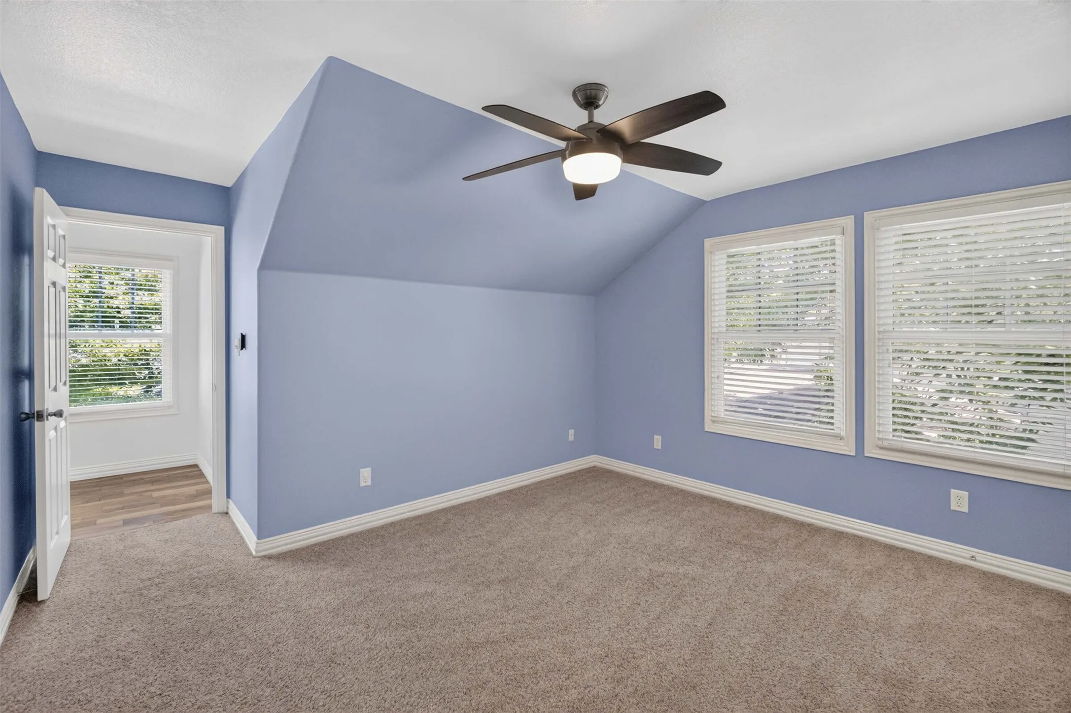 Carpeted room featuring a ceiling fan, two windows with blinds, an additional window in an alcove, and wood-finish flooring in the alcove