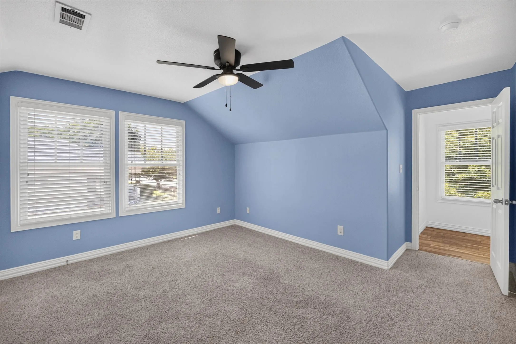 Carpeted flooring, sloped ceiling, dual windows, ceiling fan, and wood-finish flooring at the doorway