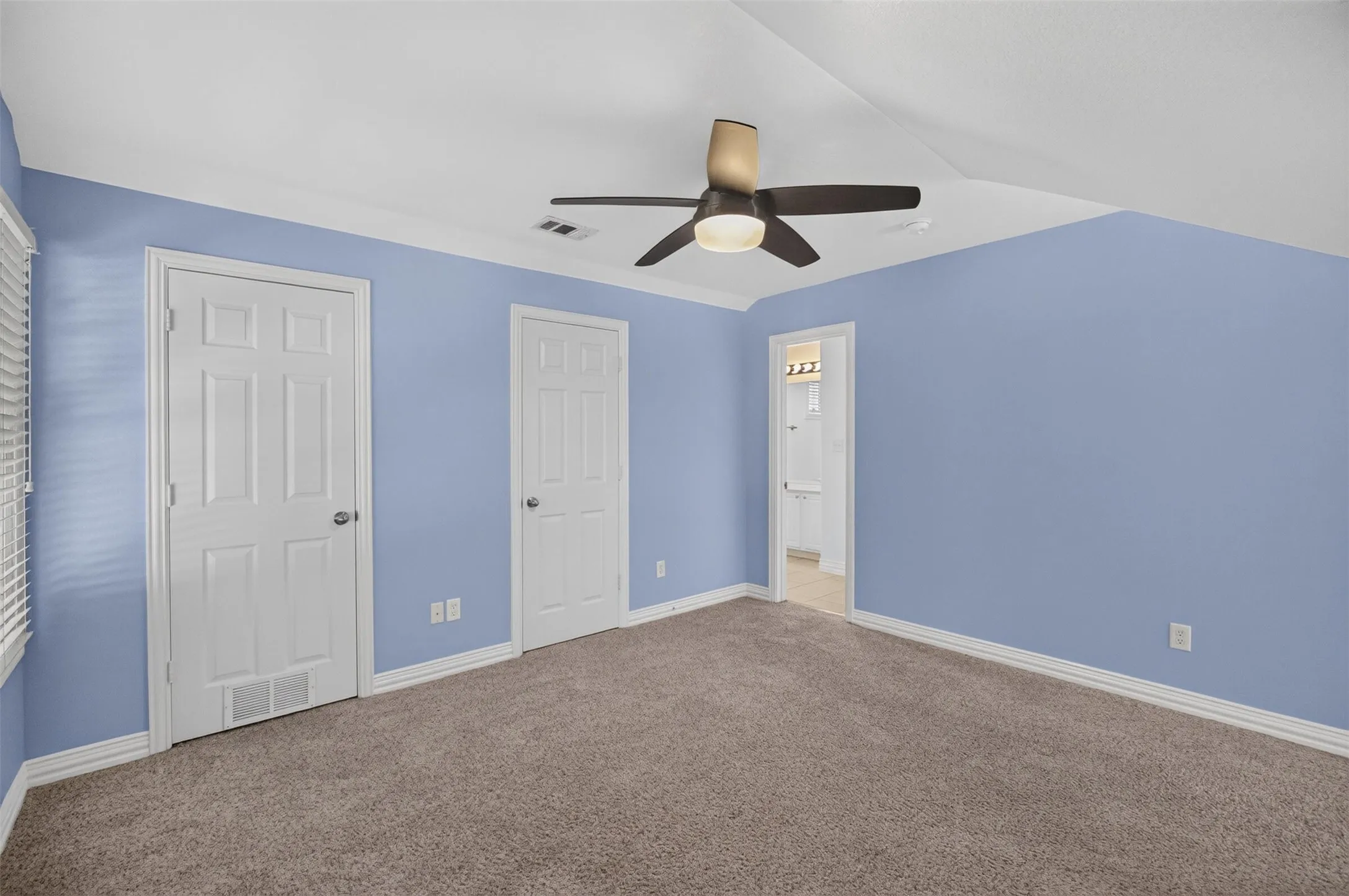 Carpeted room featuring a ceiling fan with integrated lighting, two paneled doors, and a window with blinds