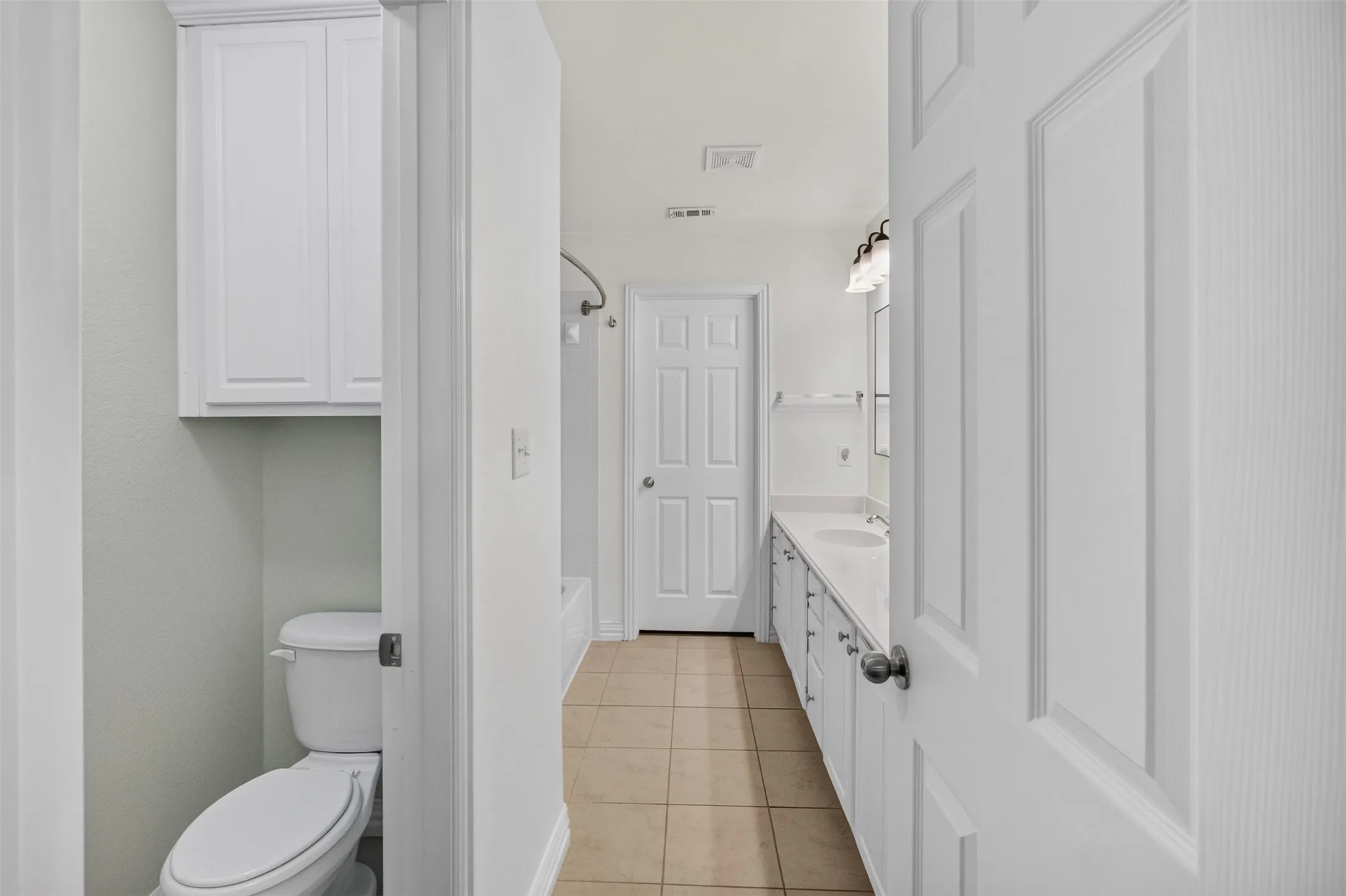 White cabinetry, neutral tile flooring, vanity with dual sinks, overhead light fixture, and white interior doors