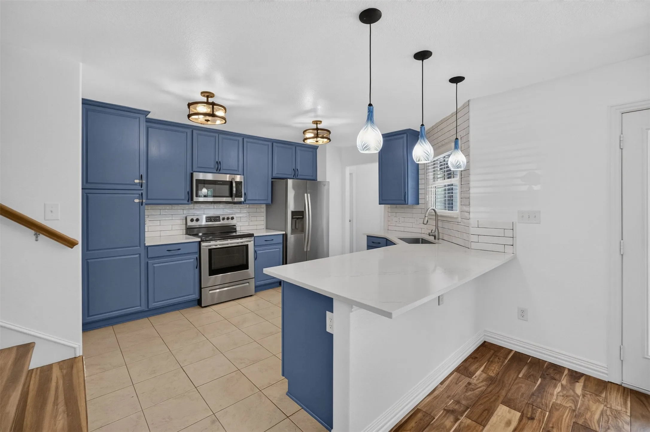 Kitchen featuring blue cabinetry, stainless steel appliances, white countertop, white subway tile backsplash, and tile flooring
