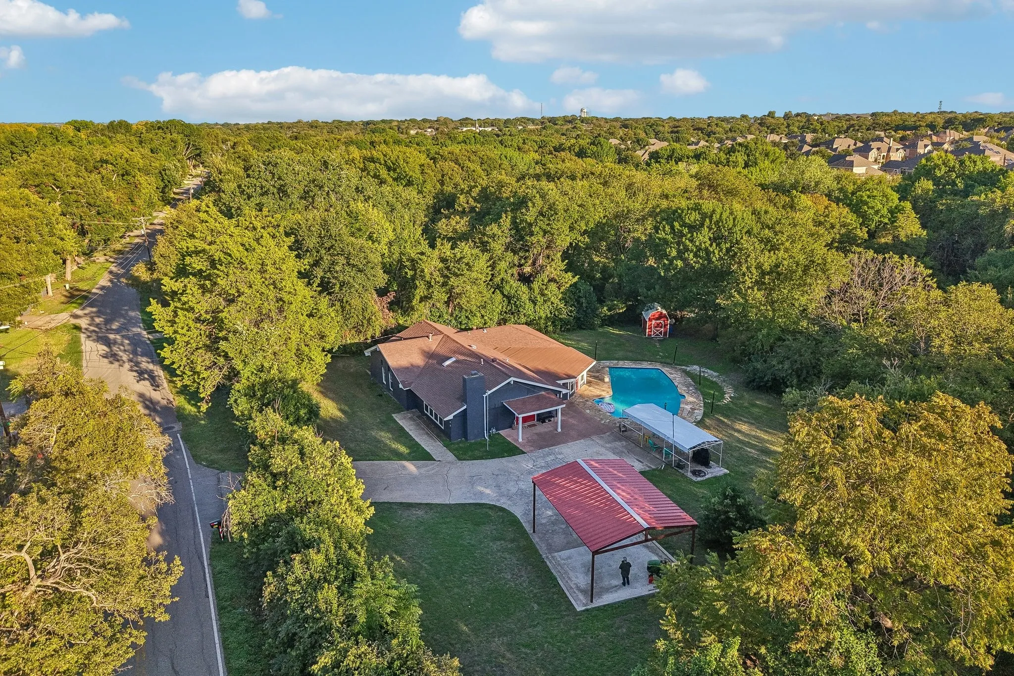 Expansive property featuring a private swimming pool, covered outdoor living space, and a red metal roof carport