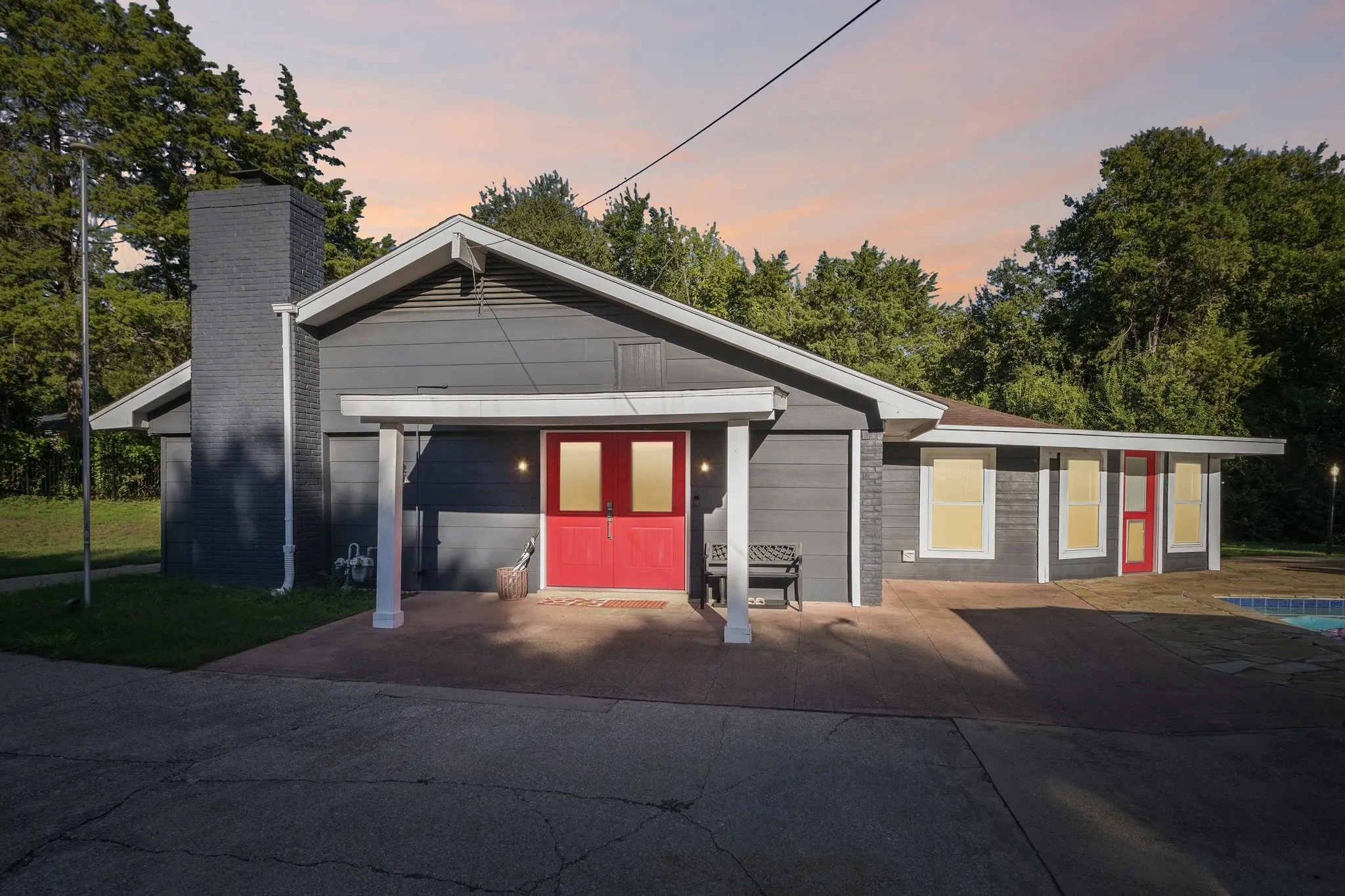 Exterior featuring a gray siding facade, prominent red entry doors, a dark brick chimney, and a concrete patio
