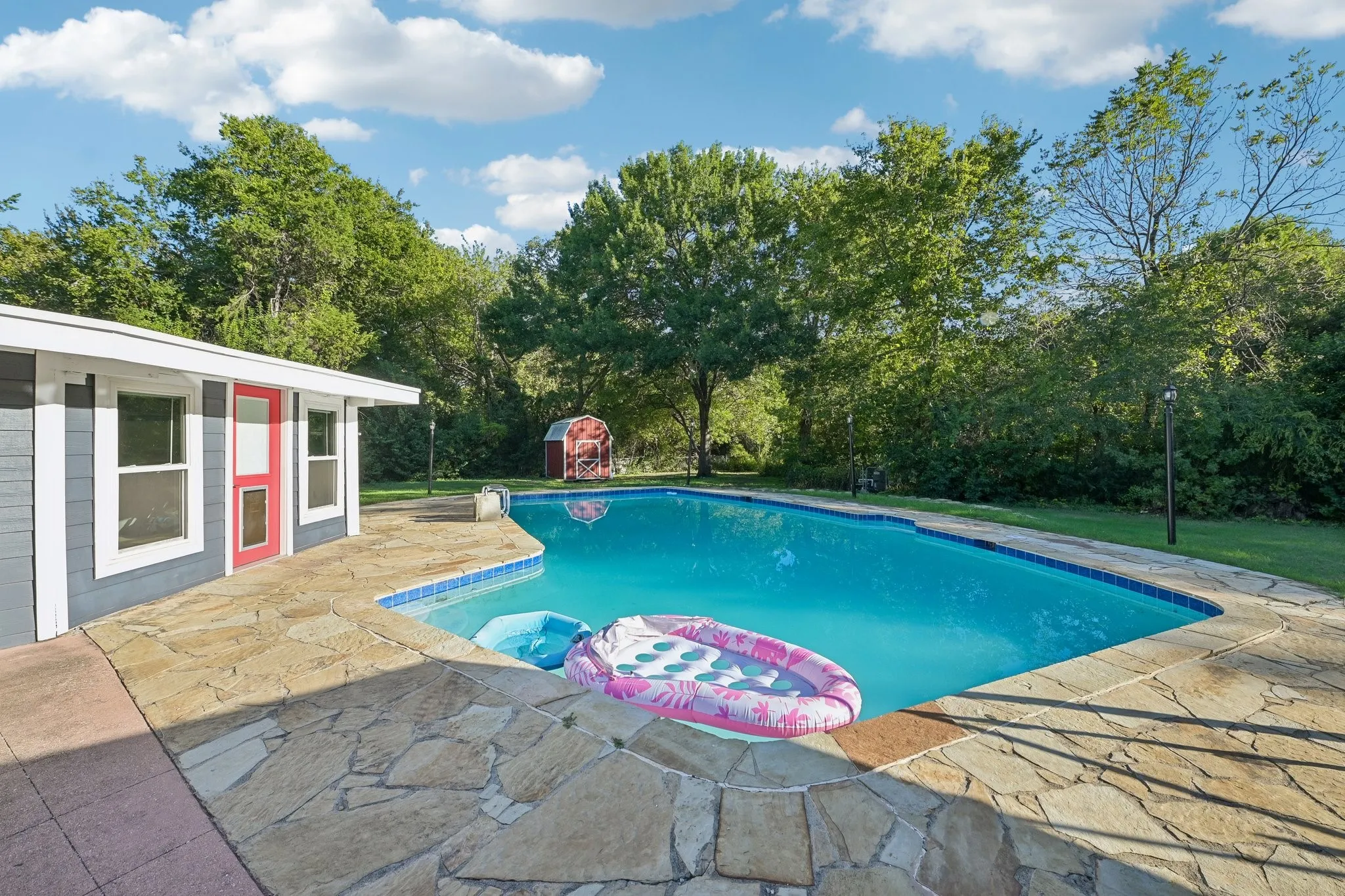 Inviting swimming pool with natural stone decking and a pool house featuring a red entry door