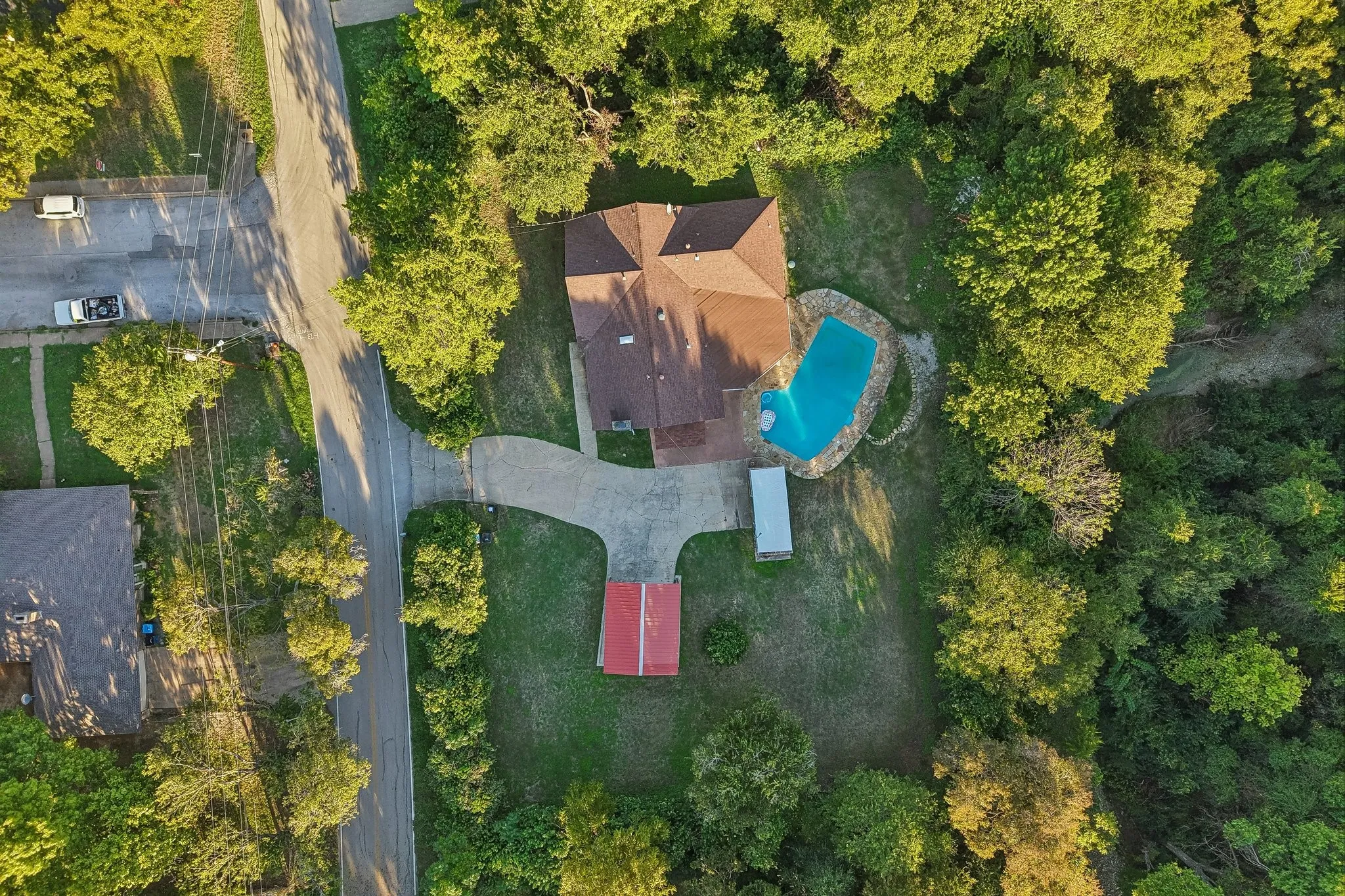 Property featuring a multi-gabled roof, an irregular-shaped swimming pool with stone coping, a detached red-roofed structure, and a paved driveway