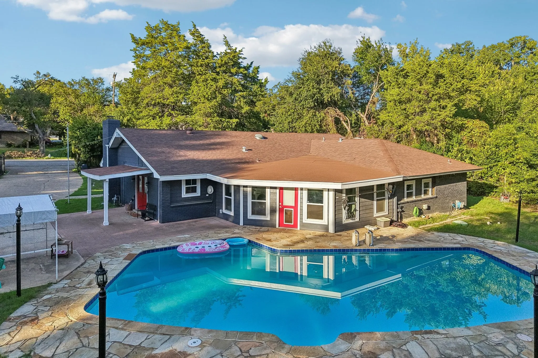 Outdoor swimming pool with integrated sun ledge, stone patio surround, and a covered entry