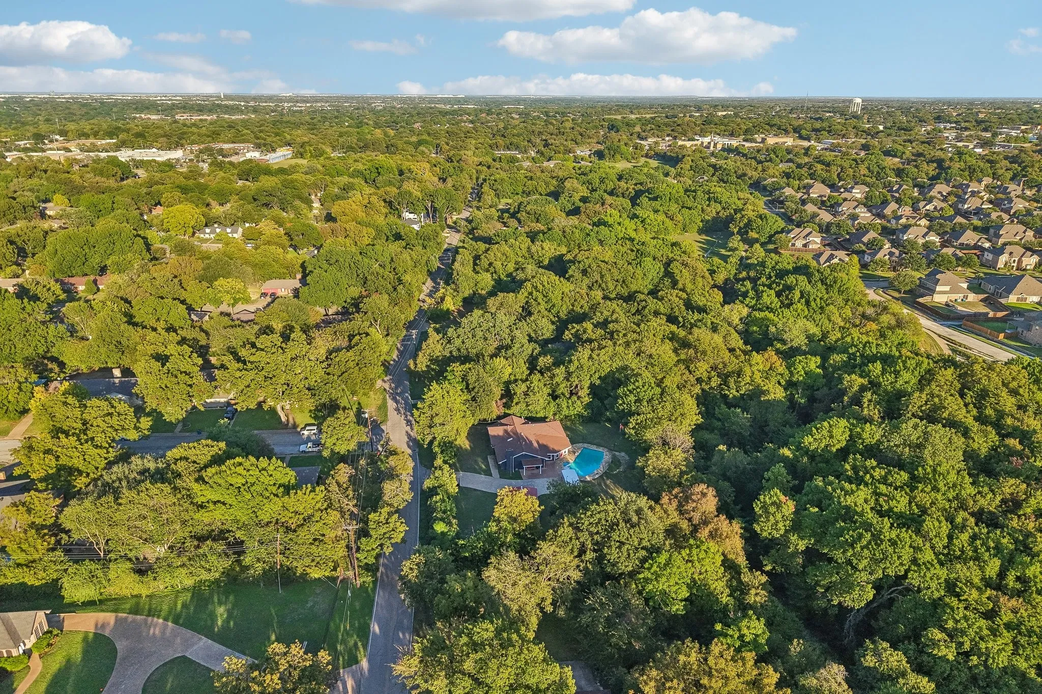 Expansive treed landscape with residential properties, including a property featuring a swimming pool